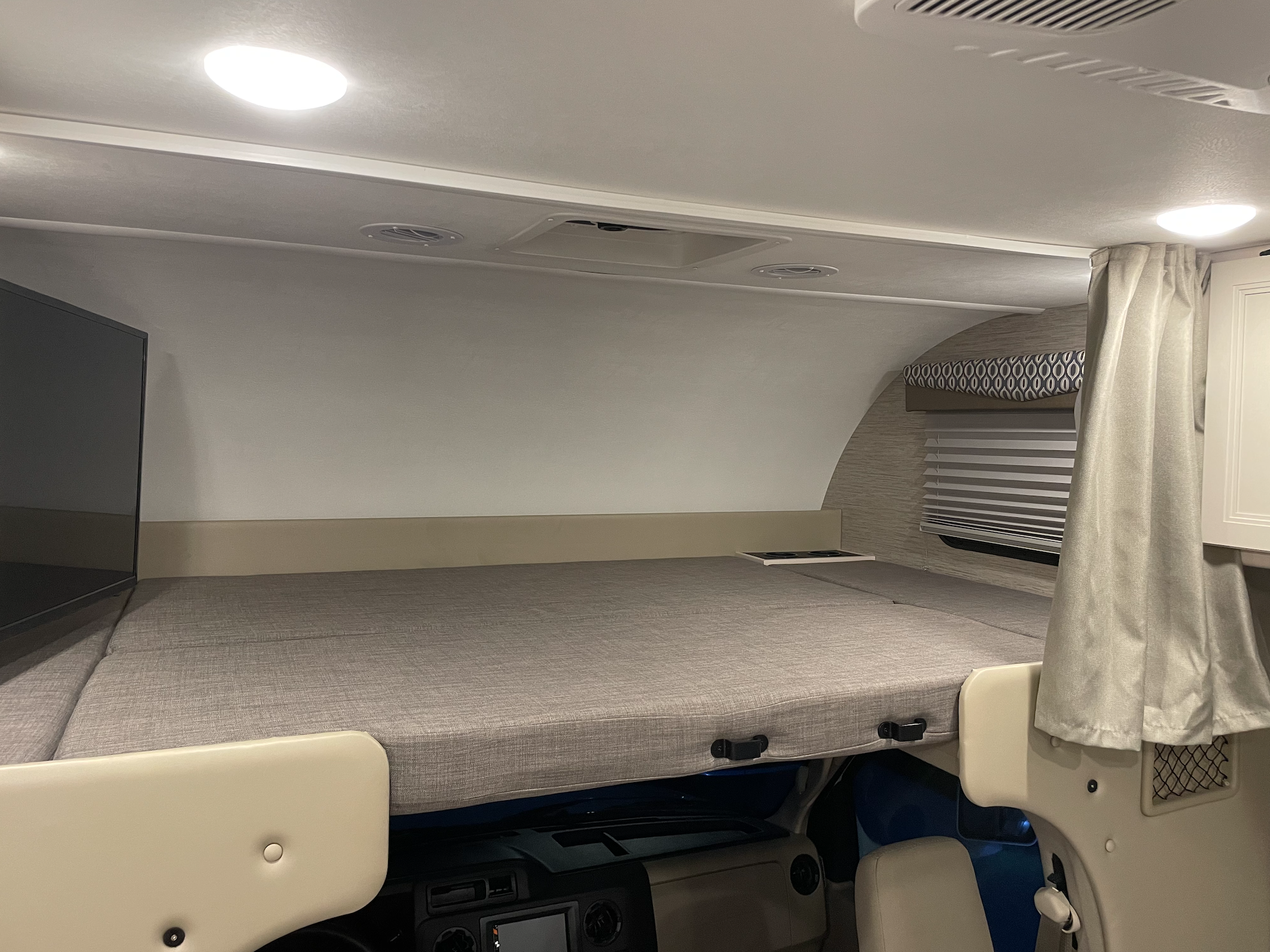RV rental: Overhead bed in a motorhome, featuring a gray mattress, TV on the left, and ceiling lights/vents.. Thor Motor Coach Freedom Elite 2022