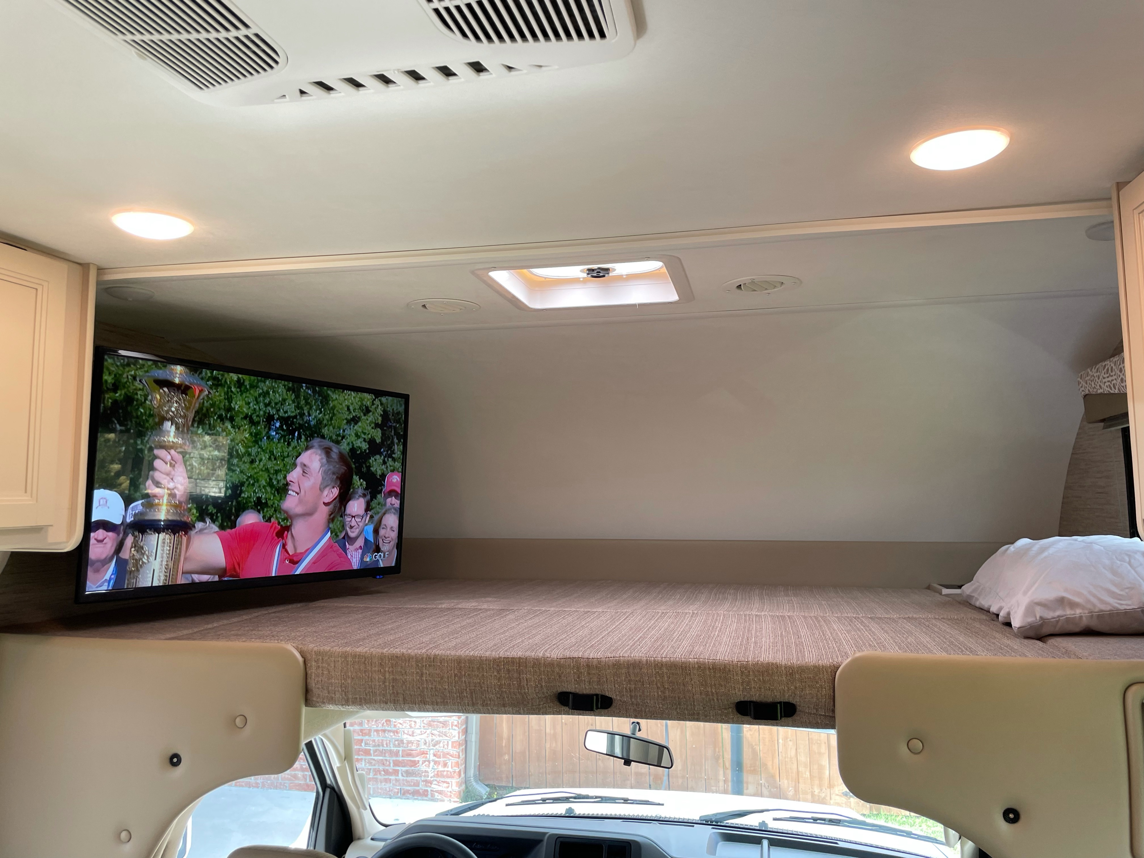 Cozy RV rental bunk with TV showing golf, perfect for relaxing after travel. Features an overhead bed in a comfortable camper.. Thor Motor Coach Freedom Elite 2022