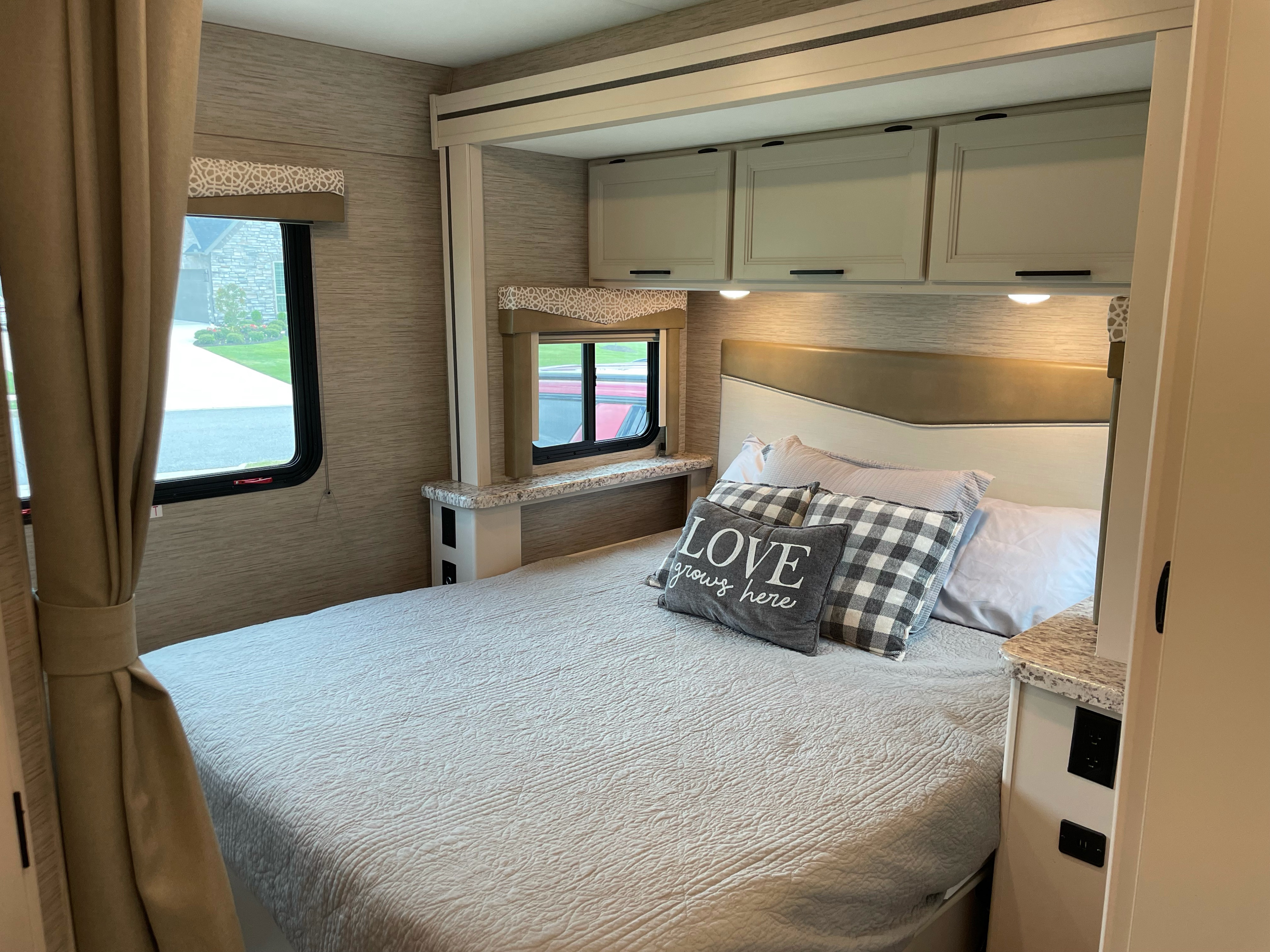 Cozy RV rental bedroom: bed, patterned pillows, storage cabinets, windows, and practical shelf with outlets.. Thor Motor Coach Freedom Elite 2022