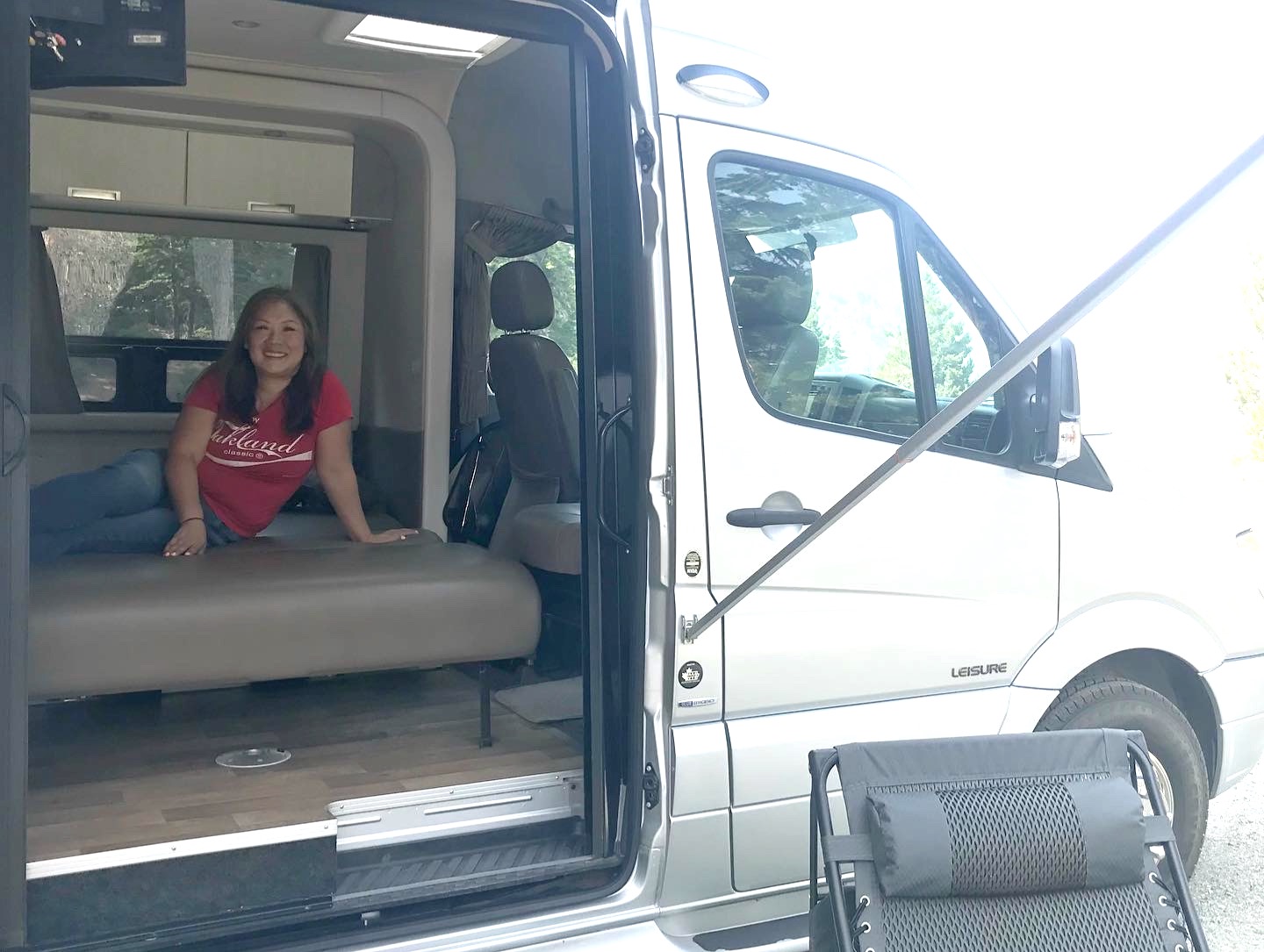 Woman relaxes in a comfortable rv rental camper van, enjoying the spacious interior, open door, and outdoor setup.. Leisure Travel Free Spirit 2013