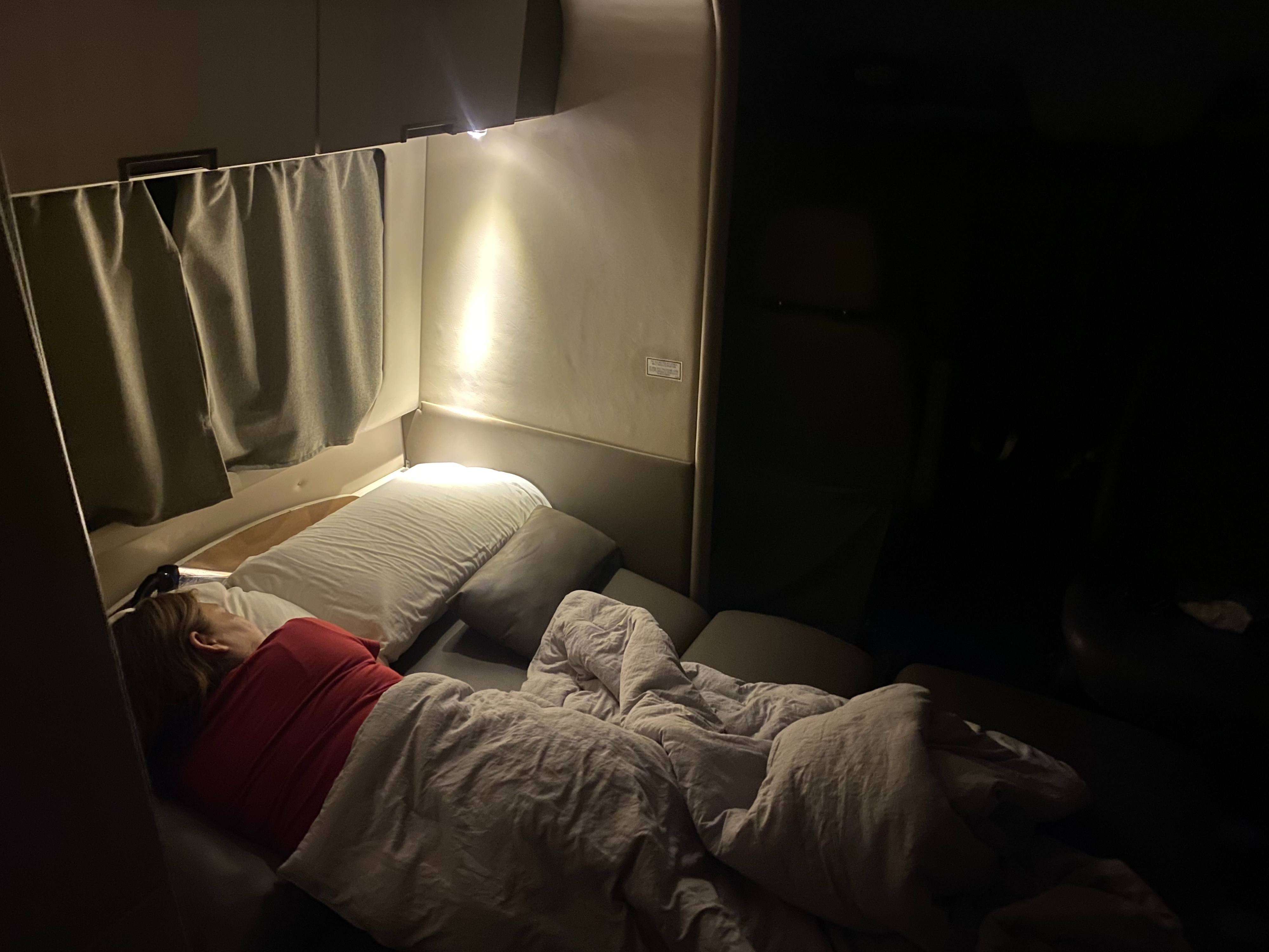 Inside a cozy RV rental, a person in a red shirt sleeps peacefully on a bed, illuminated by a soft overhead light.. Leisure Travel Free Spirit 2013