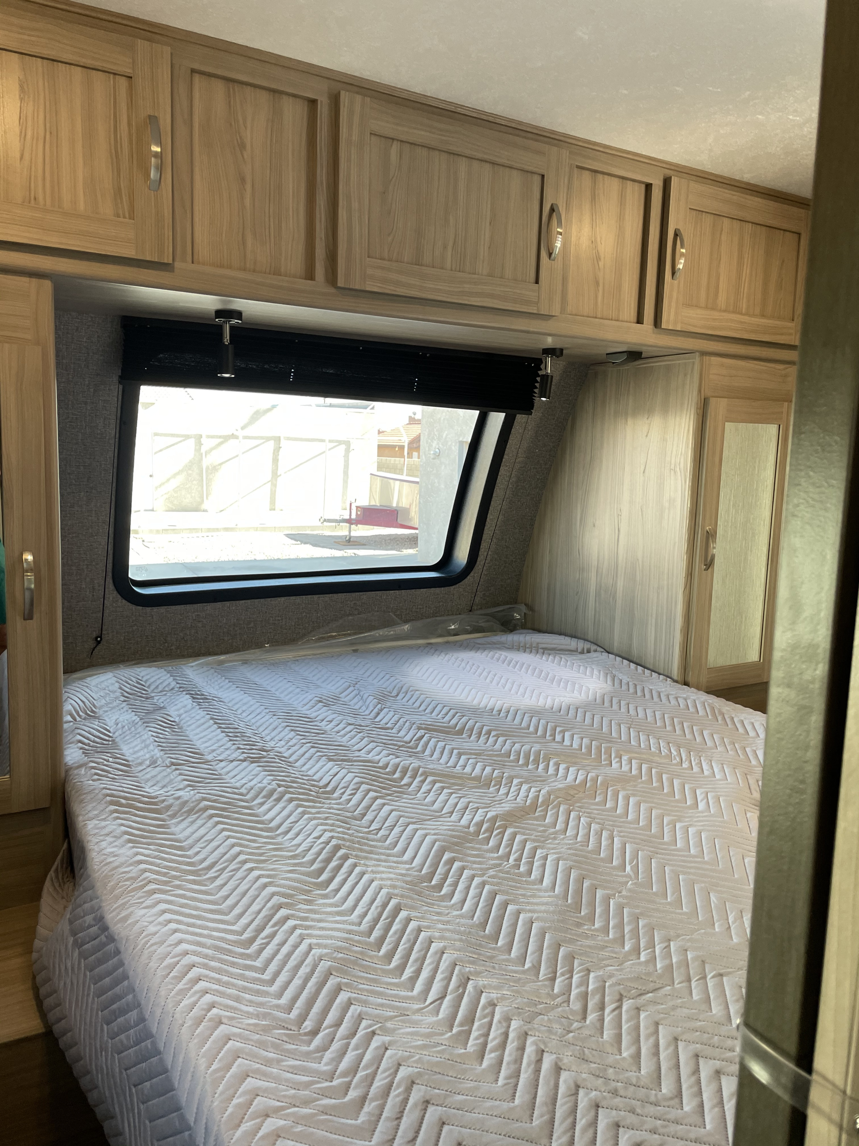 Inside an RV rental bedroom, a neatly made bed with a white chevron quilt, wood cabinets, and window is visible.. Coachmen Freedom Express 2022