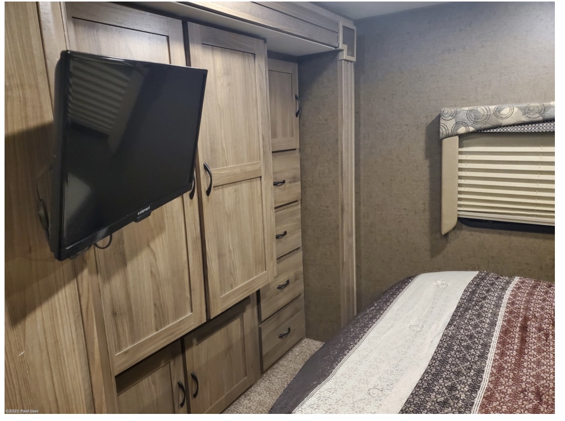 RV rental bedroom with wall-mounted TV, integrated wooden storage cabinets, and a comfortable bed.. Coachmen Freelander 31BH 2017