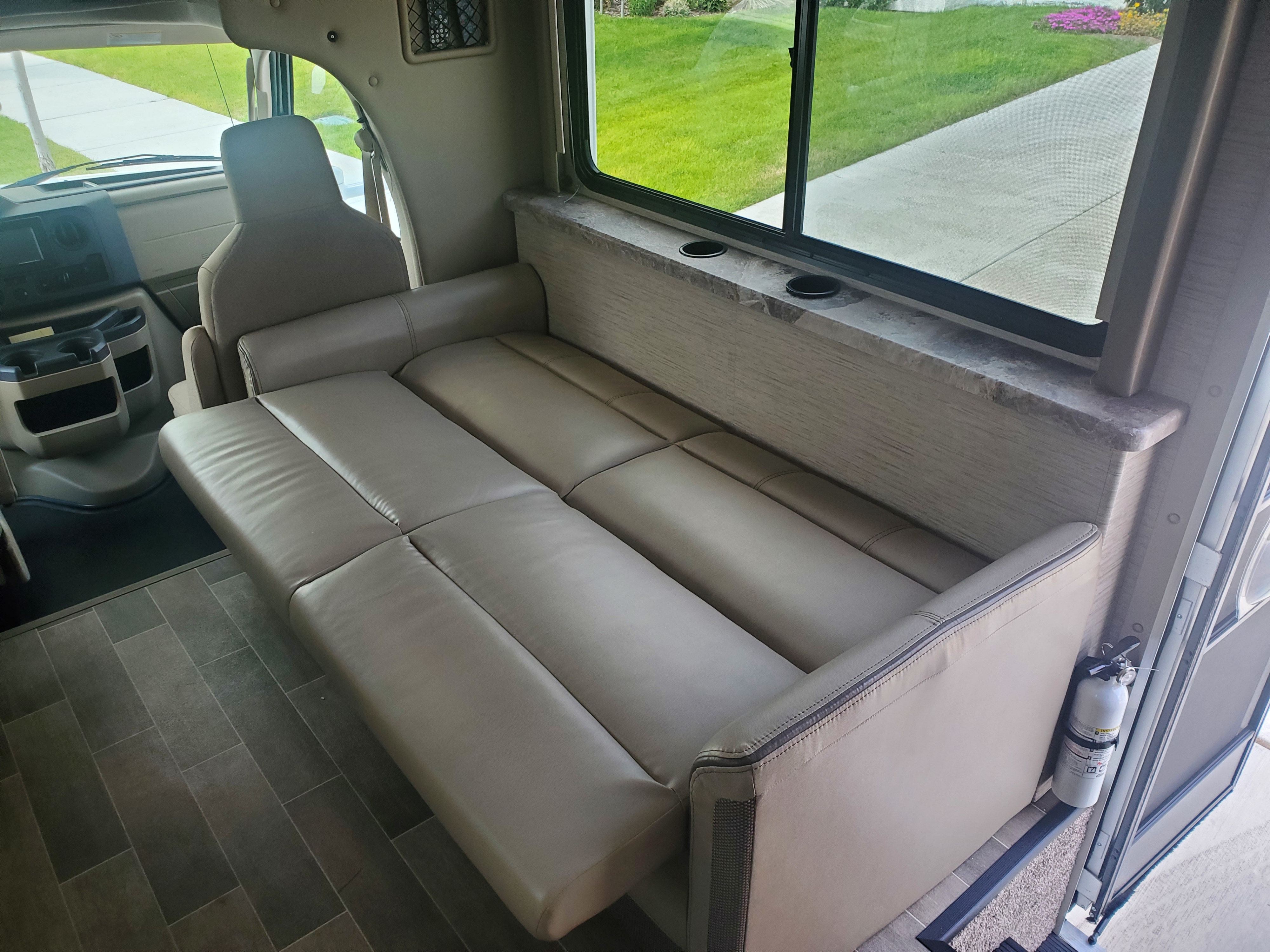 RV rental interior shows a comfortable convertible sofa bed, driver's area, window, and safety features.. Thor Motor Coach Other 2022