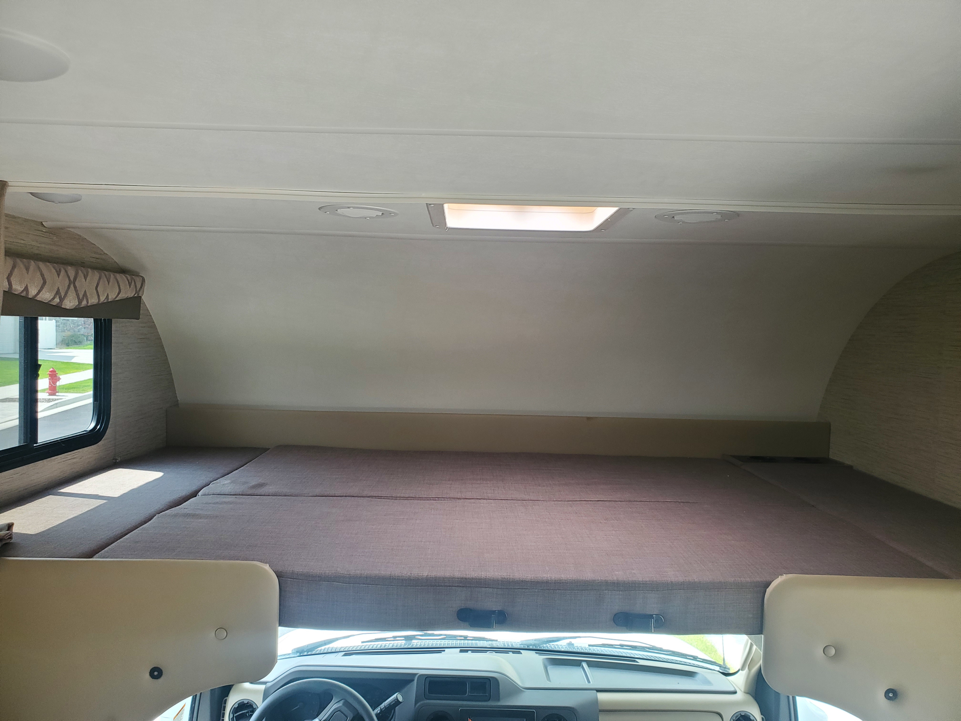 Inside a bright **rv rental**: The spacious cab-over bunk bed with a window, skylight, and dashboard view.. Thor Motor Coach Other 2022