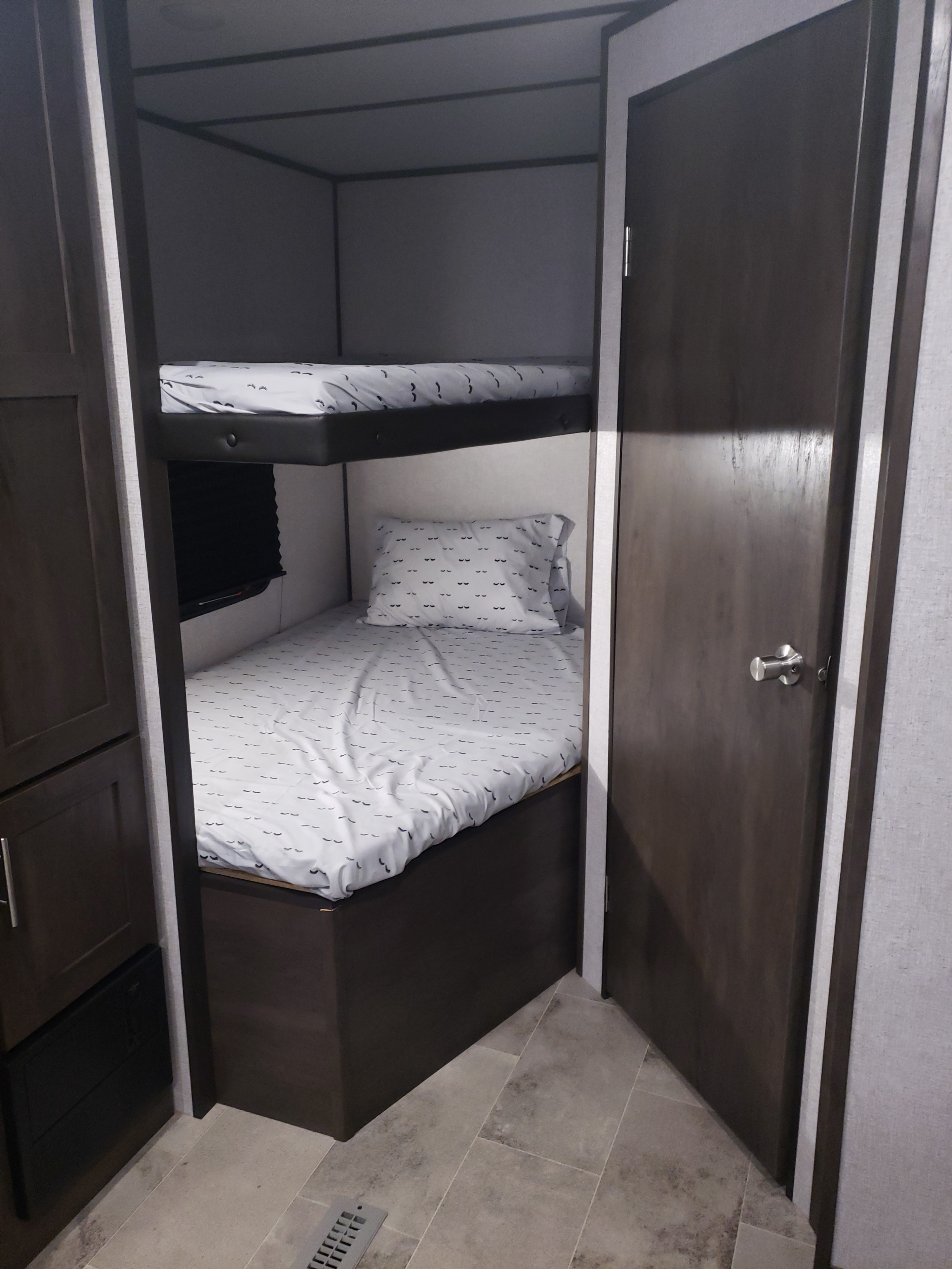 Inside this RV rental: cozy bunk beds with unique eyelash-patterned sheets, framed by dark wood storage and a door.. Dutchmen Coleman 2021