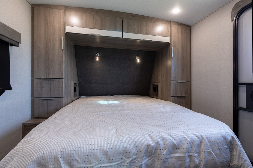 Spacious and modern RV rental bedroom featuring a full bed, built-in storage, and ambient lighting.. Grand Design Imagine 2022