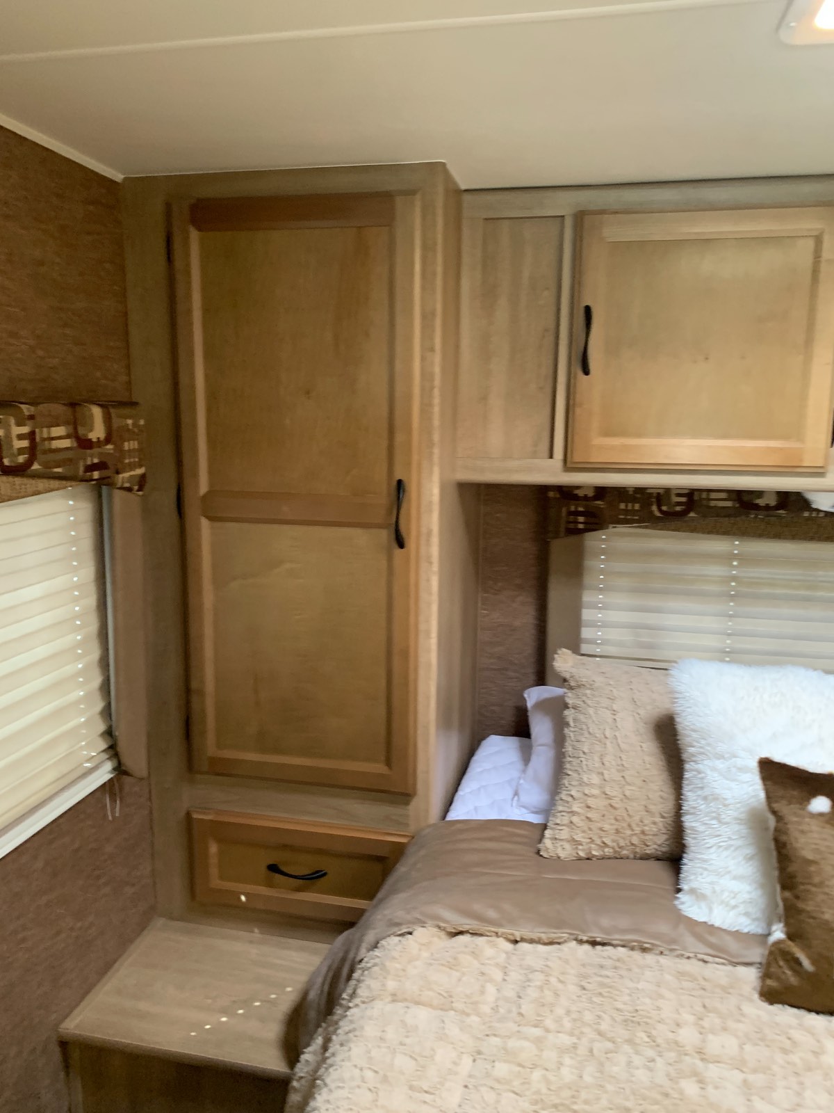 An RV rental bedroom with warm wood cabinetry, a bed with plush pillows, and pull-down blinds, offering a cozy retreat.. Coachmen Freelander 2014