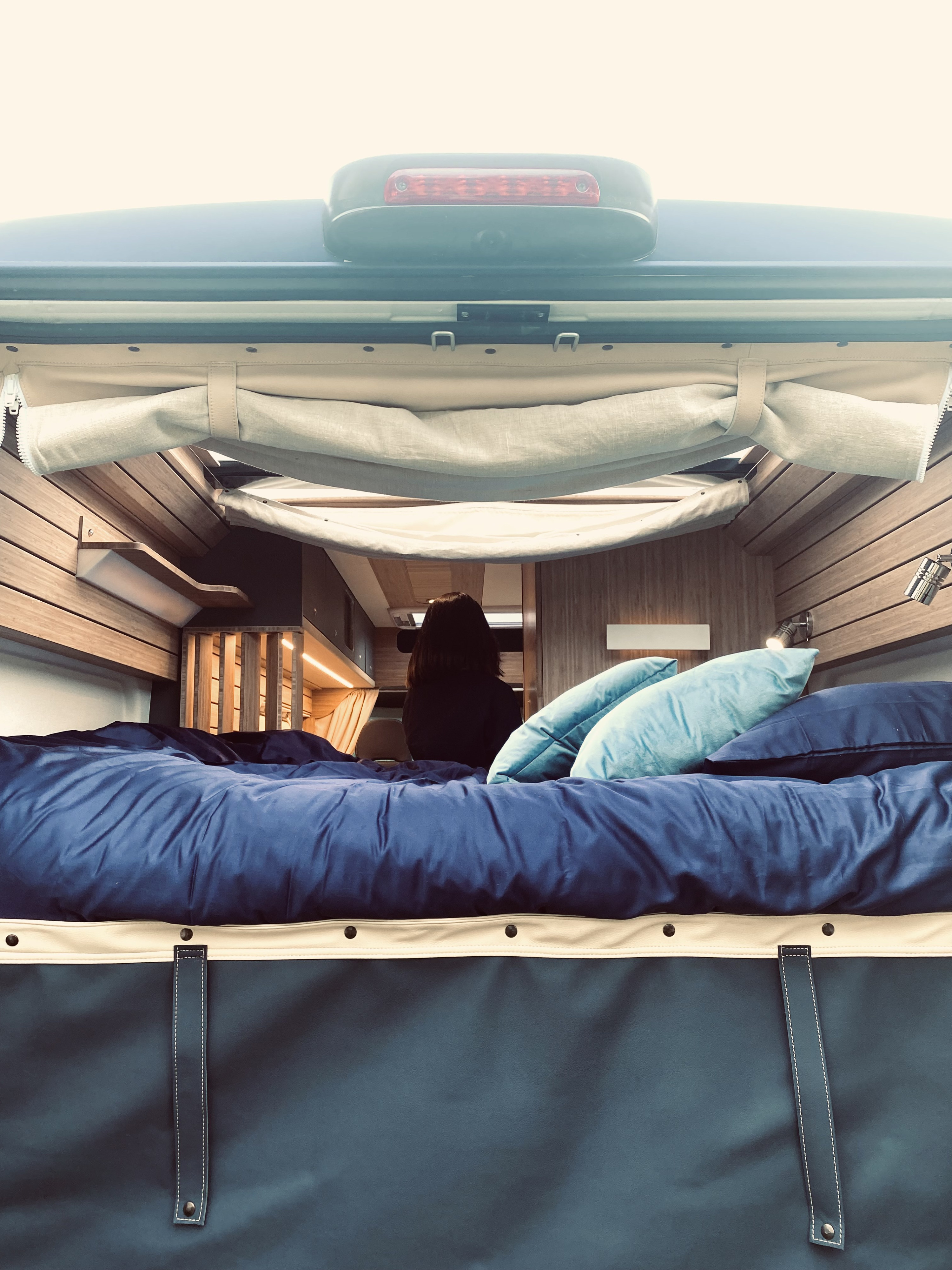 Comfortable rv rental bed in a modern camper van interior, featuring blue bedding and wooden accents. Ready for travel.. Fiat Ducato MH2 2021