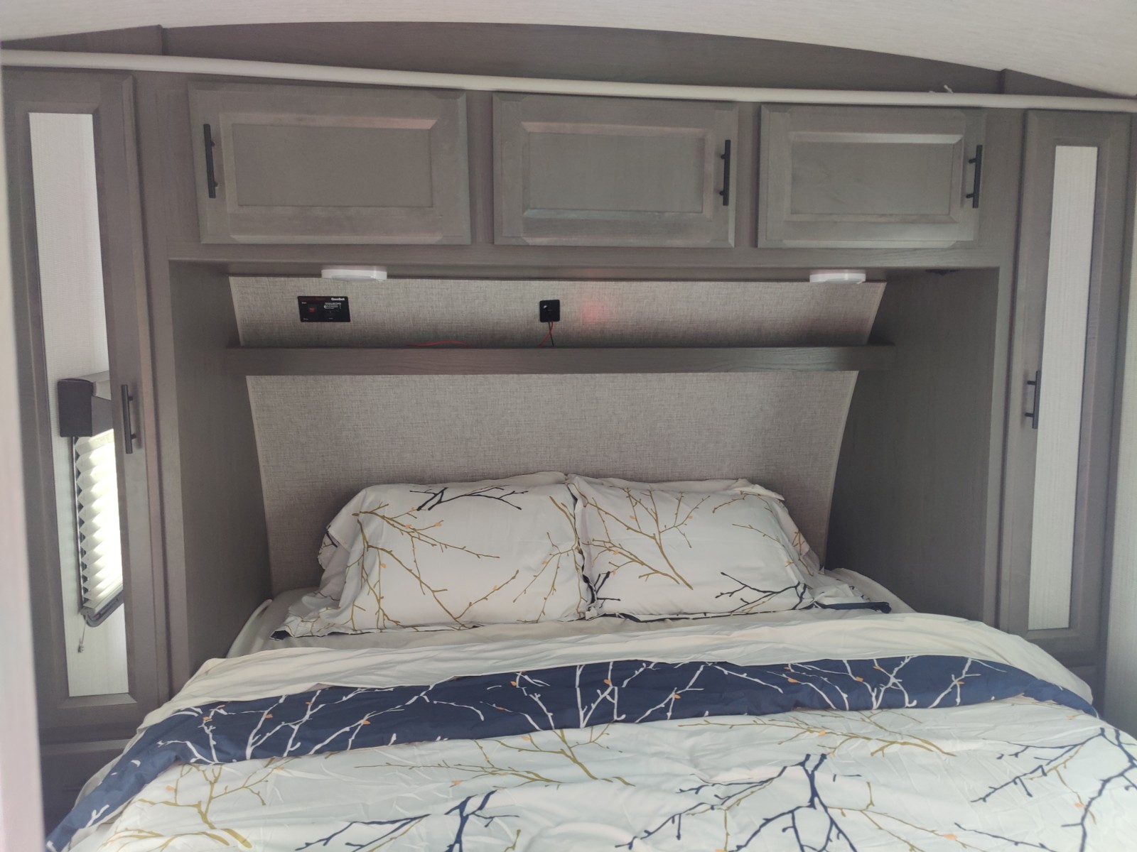Cozy RV rental bedroom featuring a bed with patterned bedding, overhead storage, and integrated lighting/outlets.. Cruiser Stryker 2313 2020