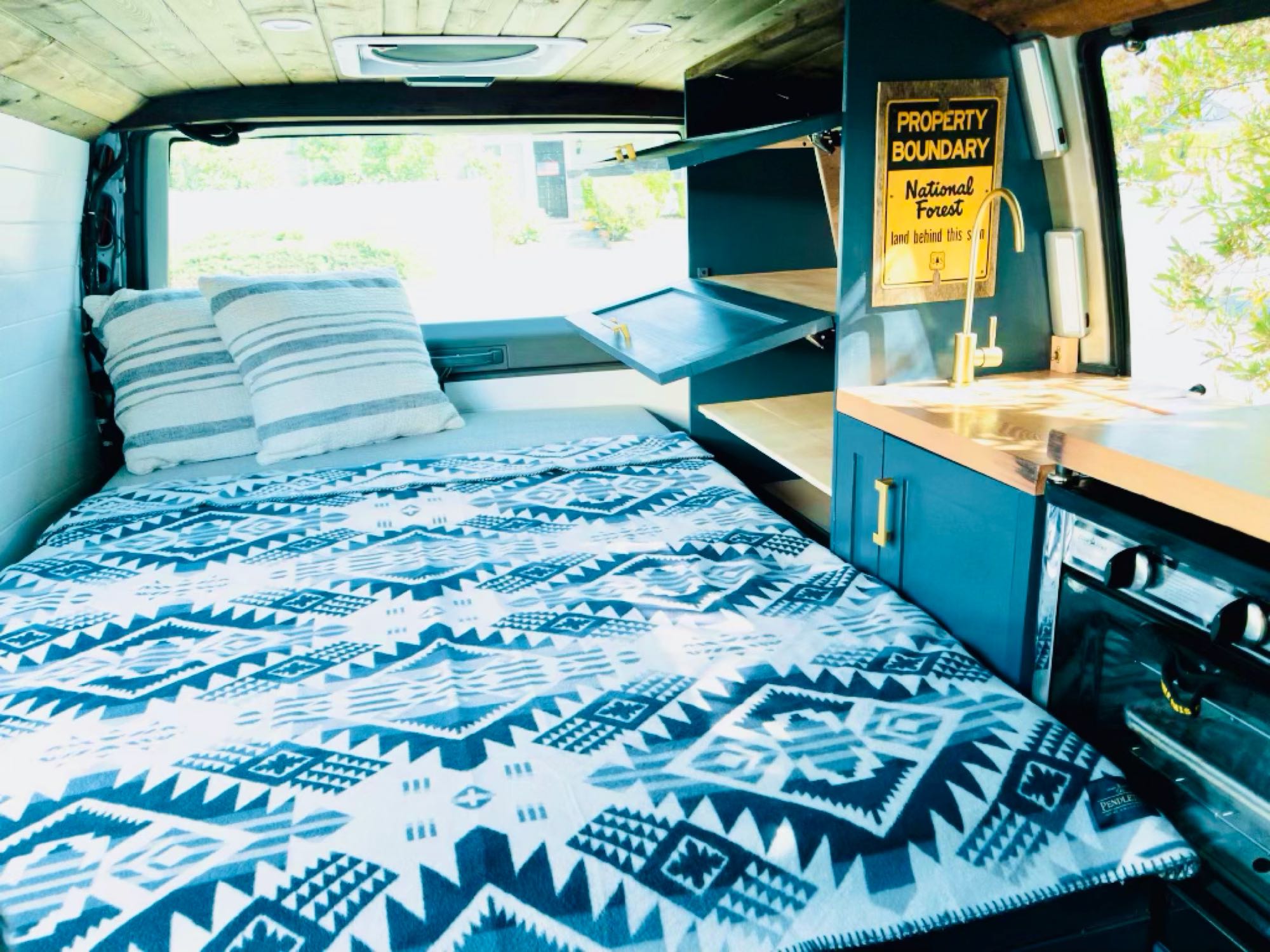 Inside a spacious **rv rental**: a comfy bed with a Pendleton blanket, small kitchen, and a fun "National Forest" sign.. Chevrolet Astro Van AWD 2003