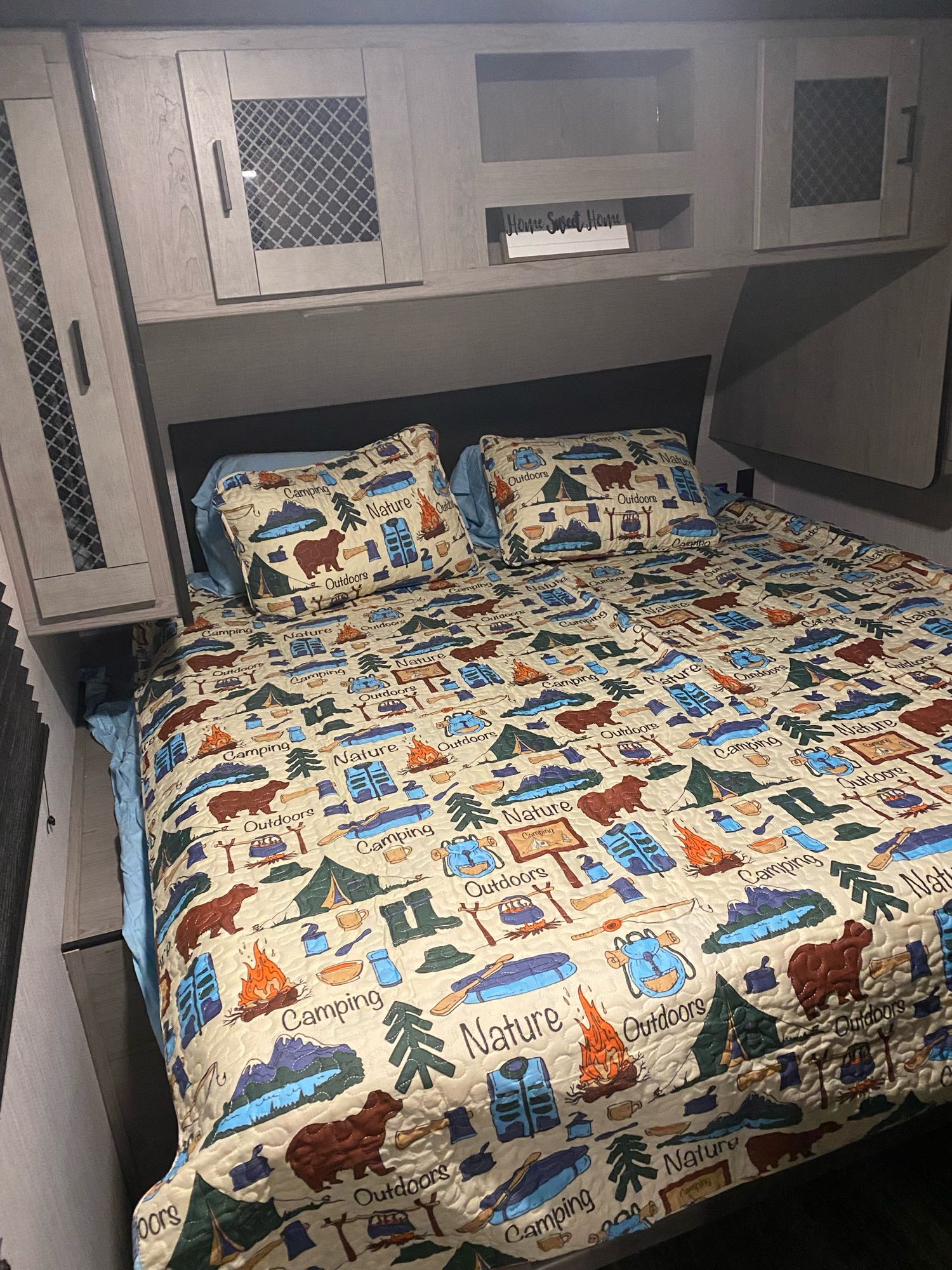 This cozy RV rental bedroom features a camping-themed quilt with bears, tents, and "Nature" designs, framed by light wood cabinets.. Heartland Mallard 2021