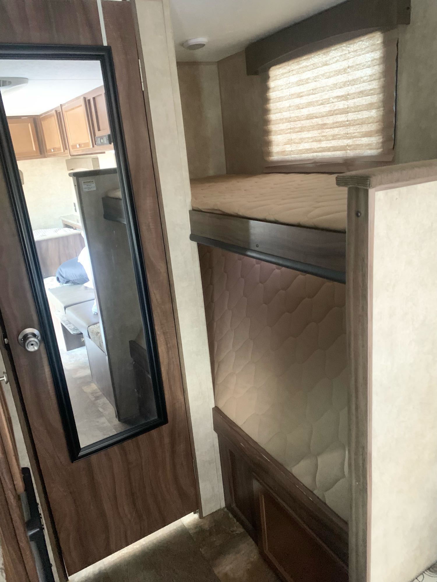 Inside an RV rental: bunk beds on the right, and a mirrored door reflecting the kitchen with cabinets, fridge, and seating.. Coachmen Clipper 2015