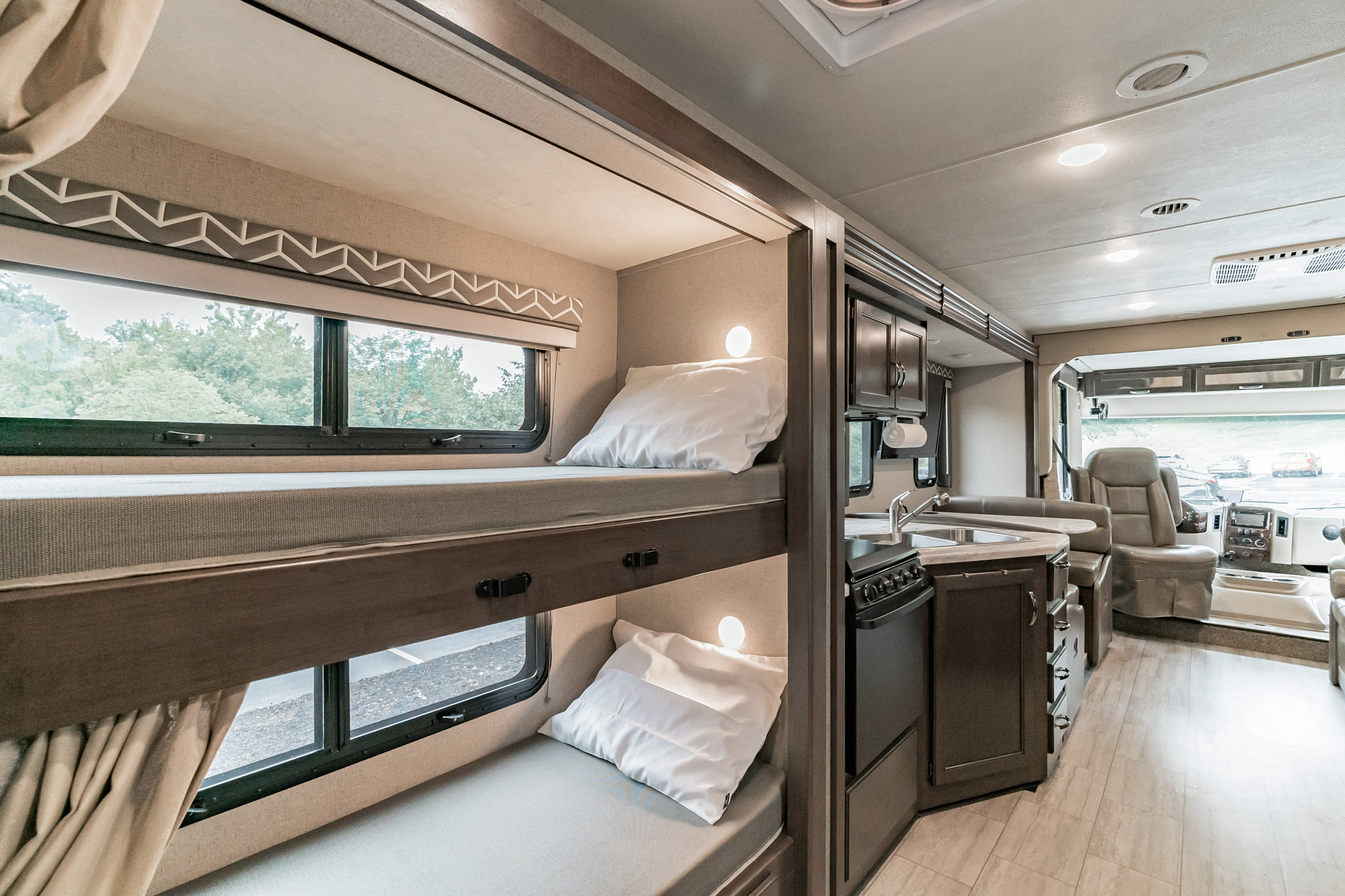 Inside a modern rv rental: full kitchen, driver's seat, and comfortable bunk beds with individual lights & windows.. Thor Motor Coach Freedom Elite 2020
