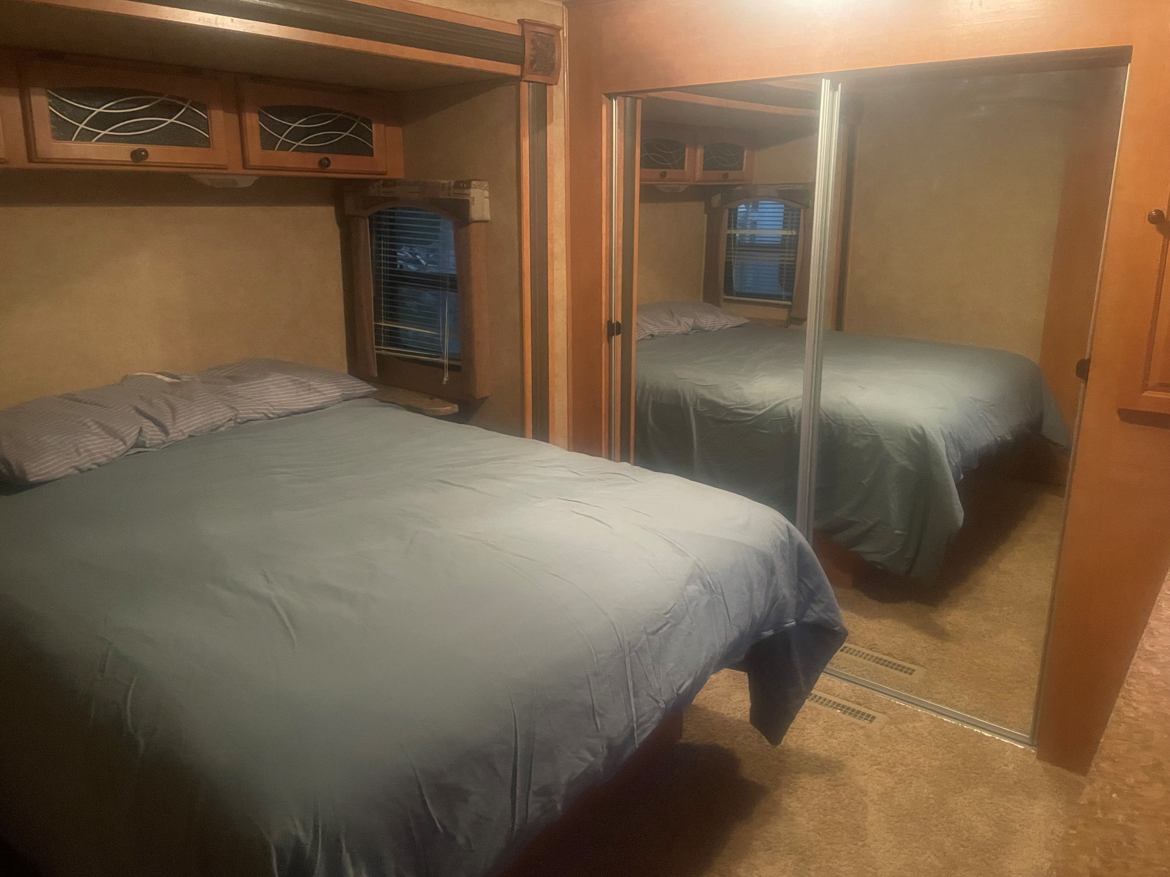 Cozy RV rental bedroom with bed, overhead cabinets, and a large mirrored closet, offering a comfortable sleeping space.. Heartland North Country Lakeside 2011