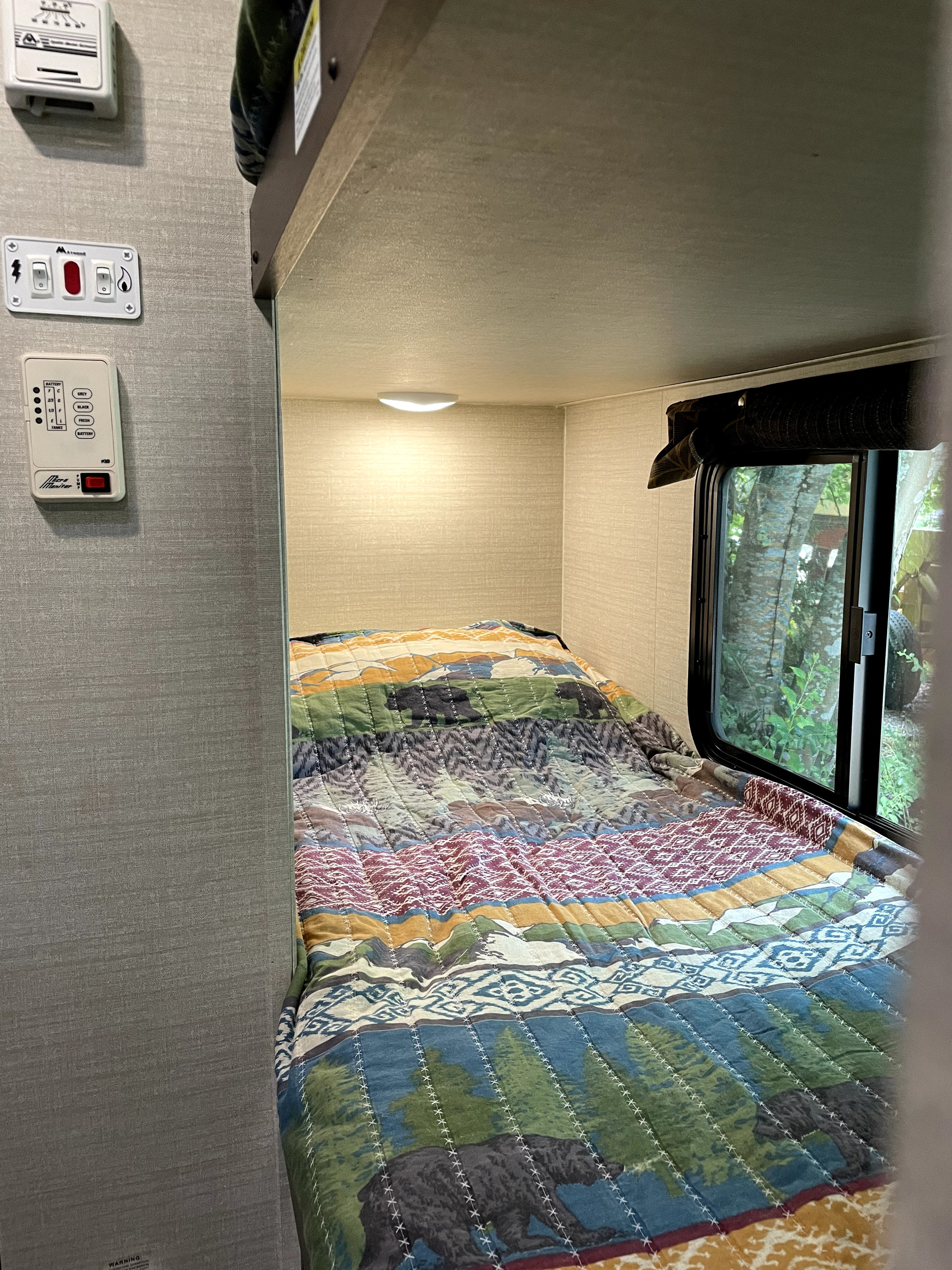 RV rental bunk bed with rustic quilt and control panel, offering a window view of nature. A cozy interior for your travels.. Keystone Bullet 2017