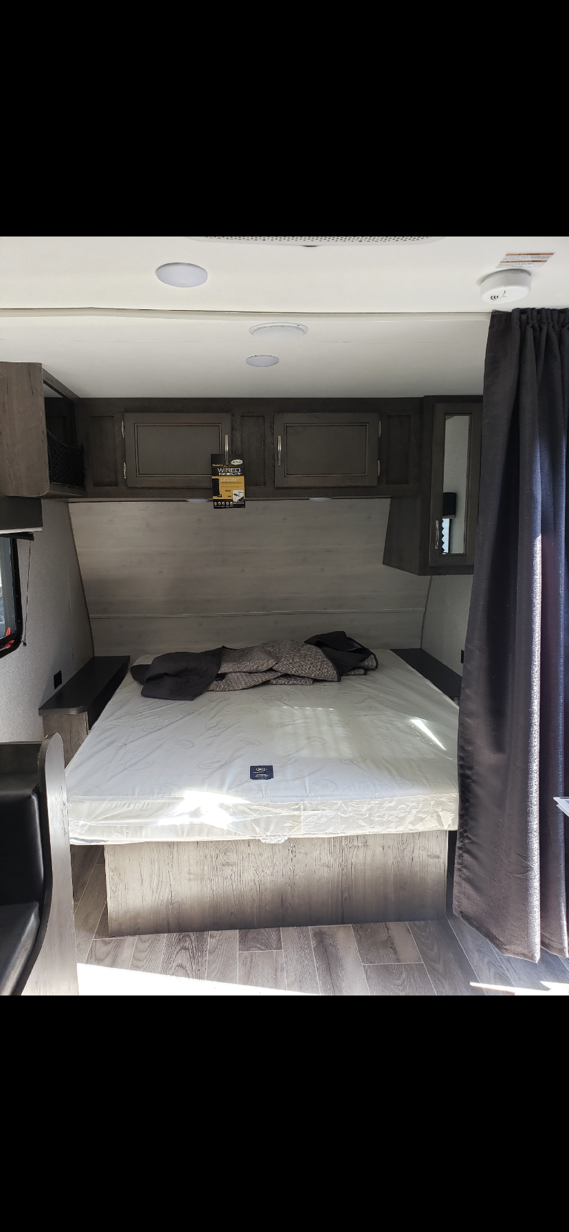 Inside an RV rental: a clean, new bedroom with a large mattress, overhead cabinets, and wood flooring. Perfect for your travels.. Jayco Jay Flight 2021