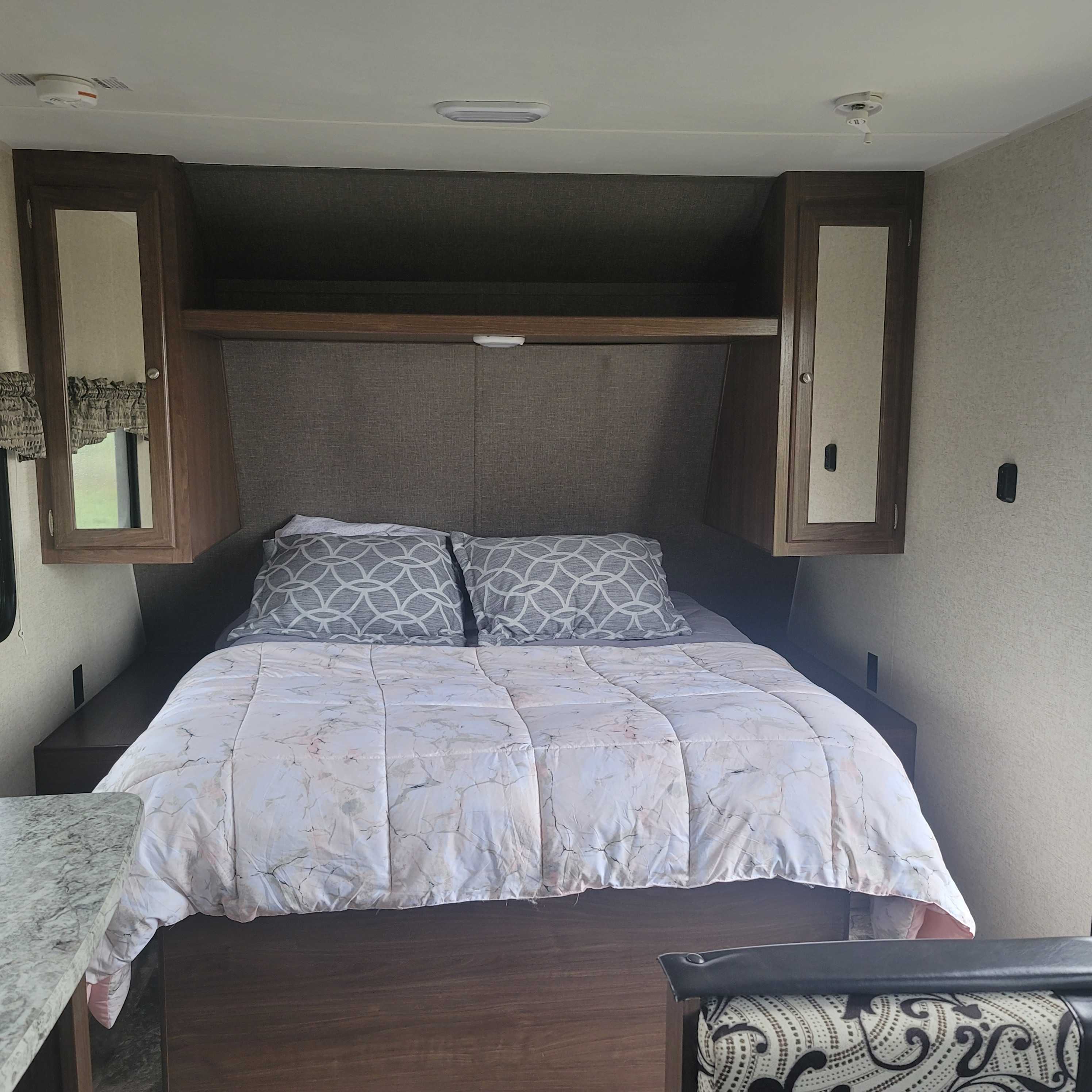 A tidy RV rental bedroom with a bed, light comforter, gray pillows, and dark wood cabinetry. Features overhead storage and ceiling lights.. Heartland Prowler Lynx 2017