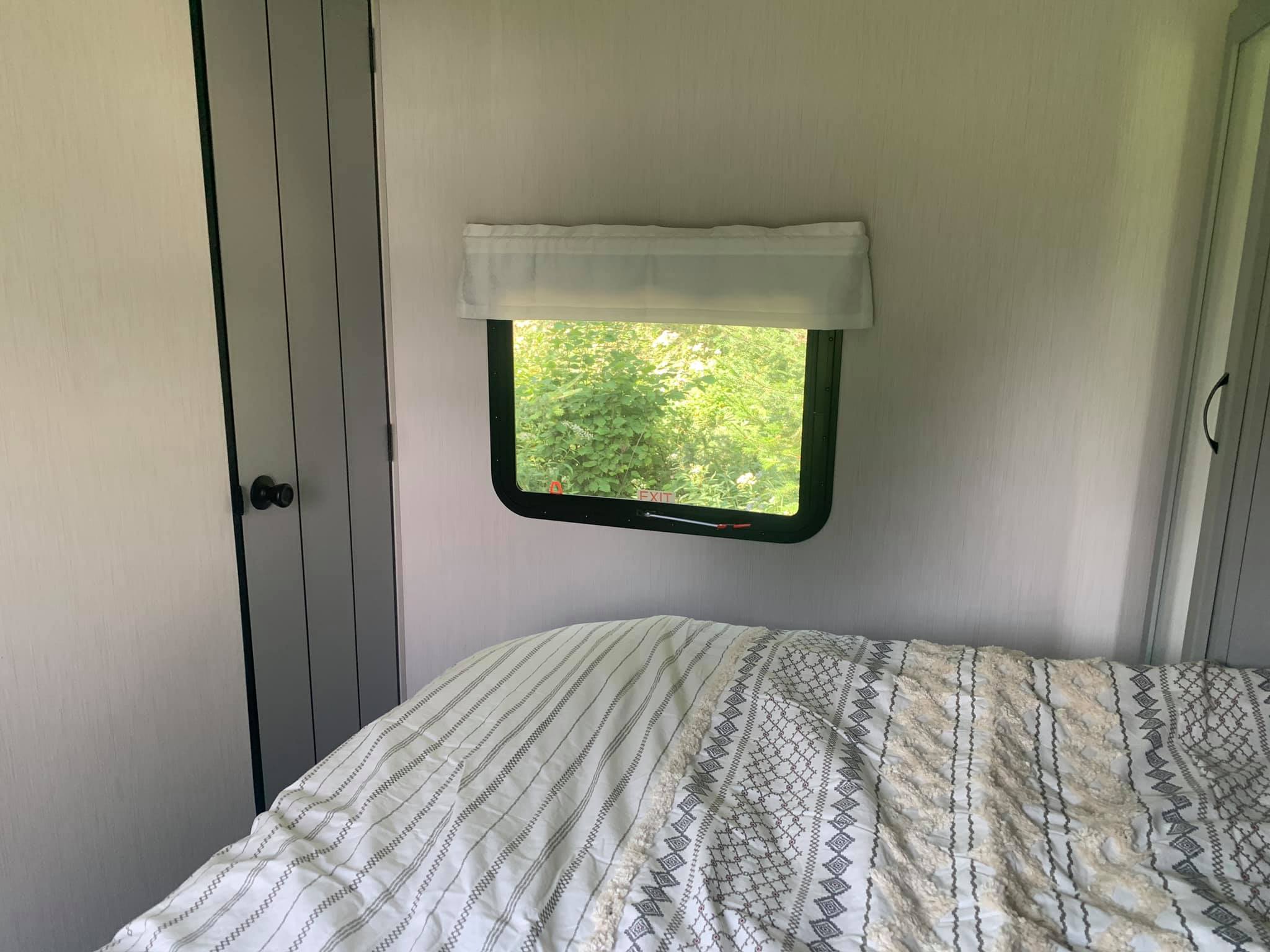 Cozy RV rental bedroom featuring a comfy patterned bed, window with green nature view, and built-in closets.. Forest River Vibe 2021
