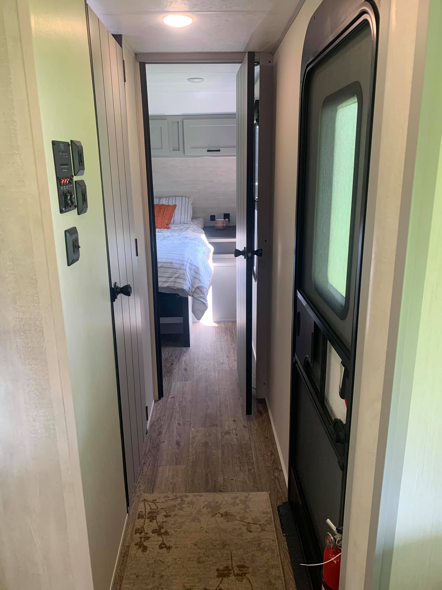 Inside this RV rental: A hallway shows a control panel, a bedroom entrance, and the main entry door with a fire extinguisher.. Forest River Vibe 2021