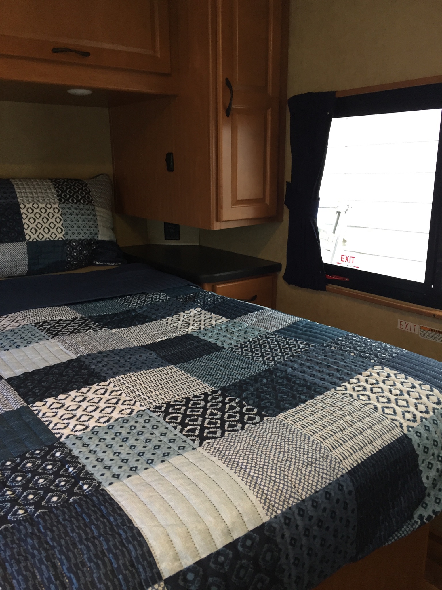 An RV rental bedroom features a comfy bed with a blue and white patchwork quilt, wood cabinets, and an emergency exit window.. Ford Majestic 2017