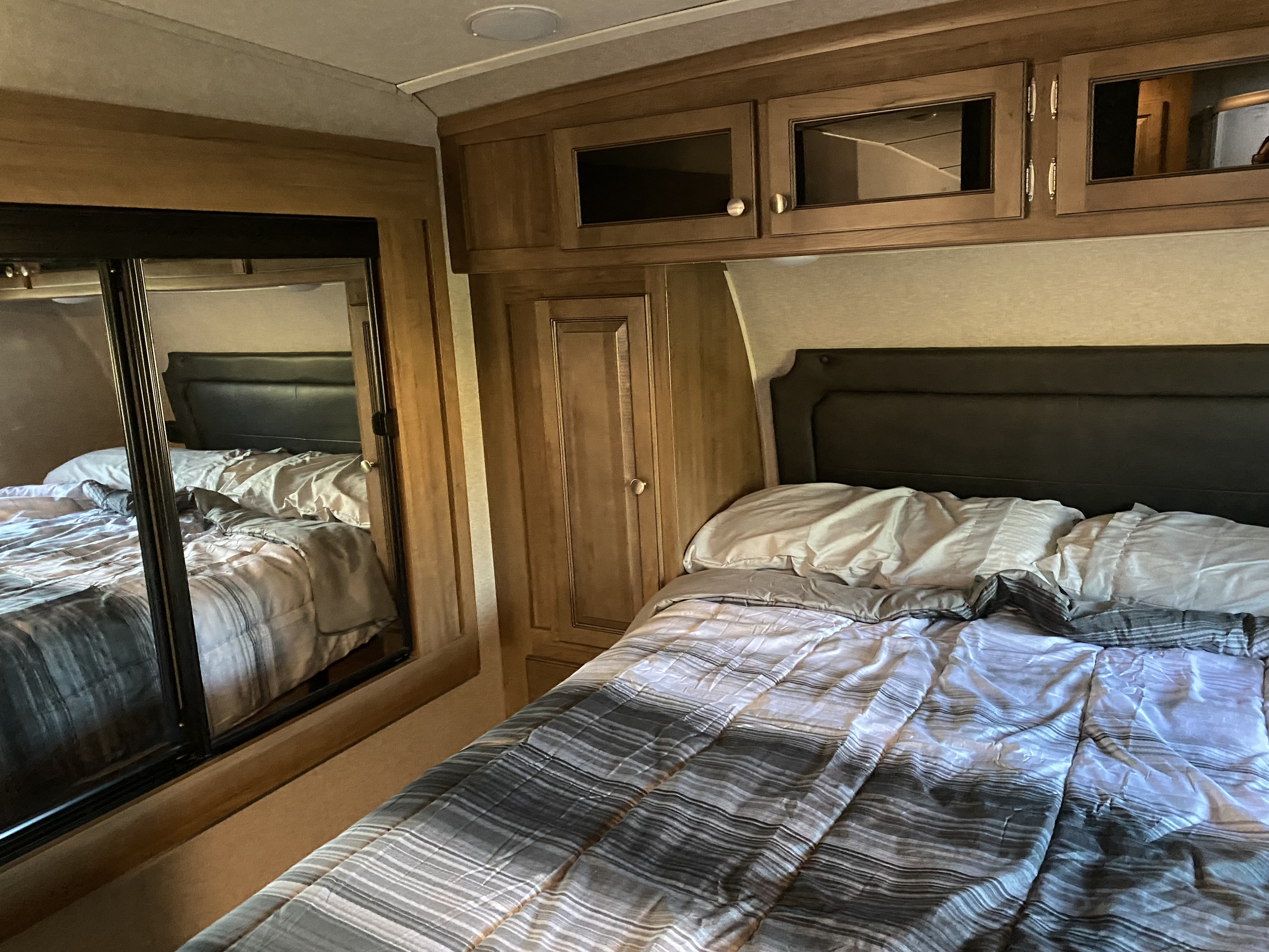 Inside an RV rental: a comfy bedroom with a striped bed, dark headboard, wood cabinetry, and a mirrored closet.. Forest River Rockwood Ultra Lite 2019