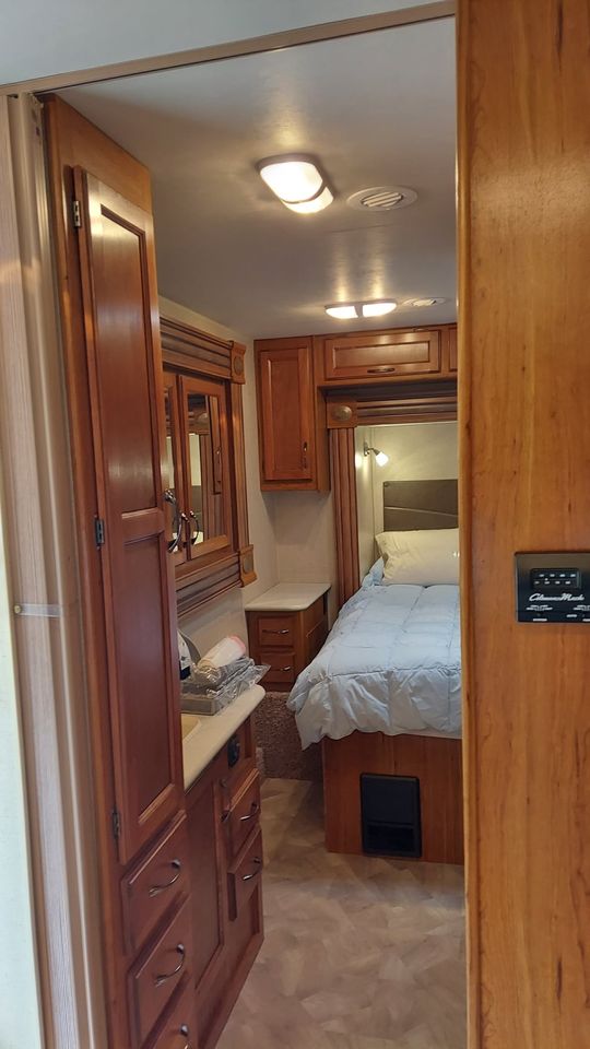 Inside an RV rental: a well-appointed bedroom with a bed and reading lights, plus a vanity area with wood cabinets.. Jayco Redhawk 2016