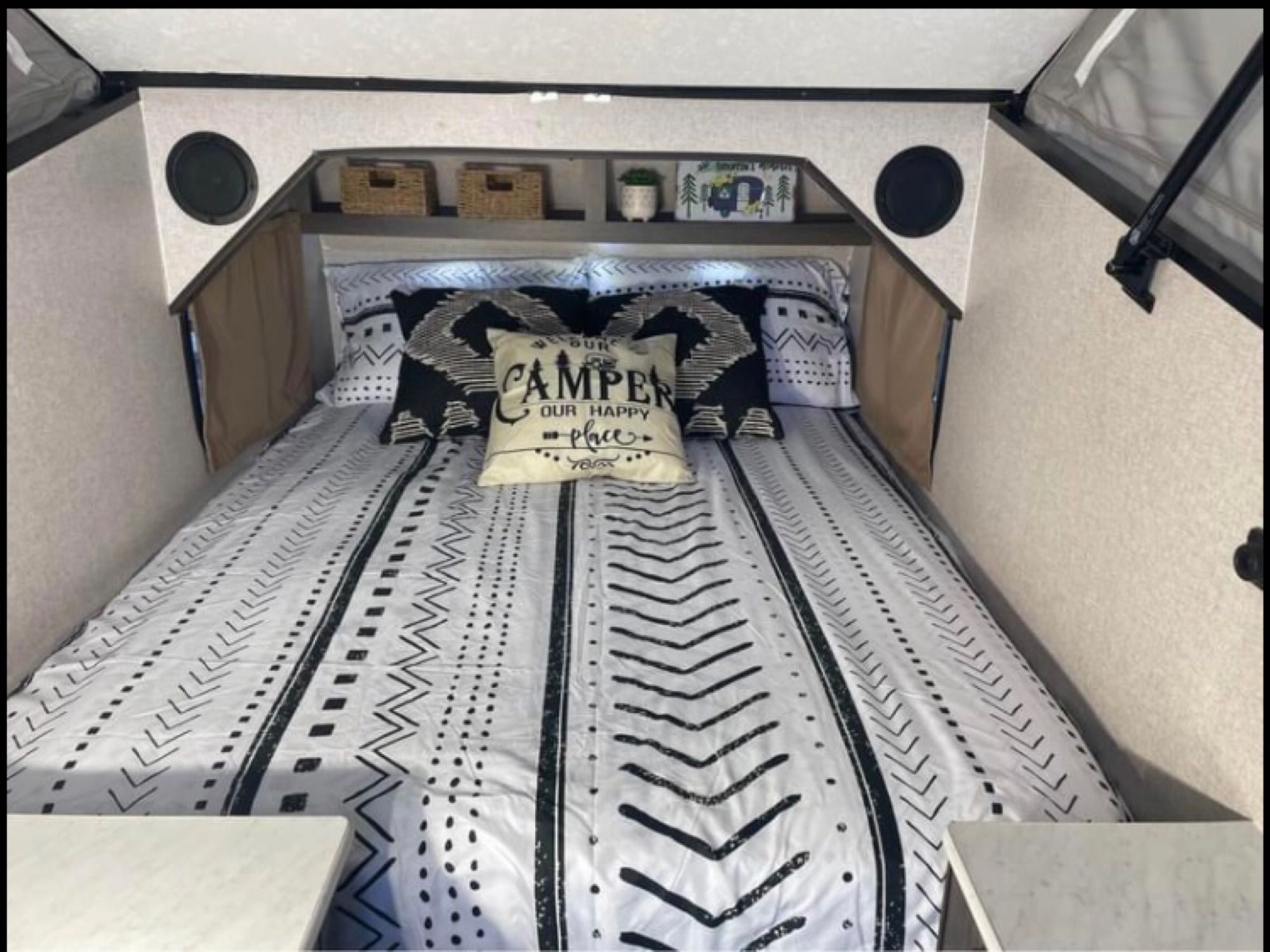 Cozy RV rental interior: A bed with black & white patterned bedding, throw pillows, overhead shelves, and built-in speakers.. Coachmen Viking 2020