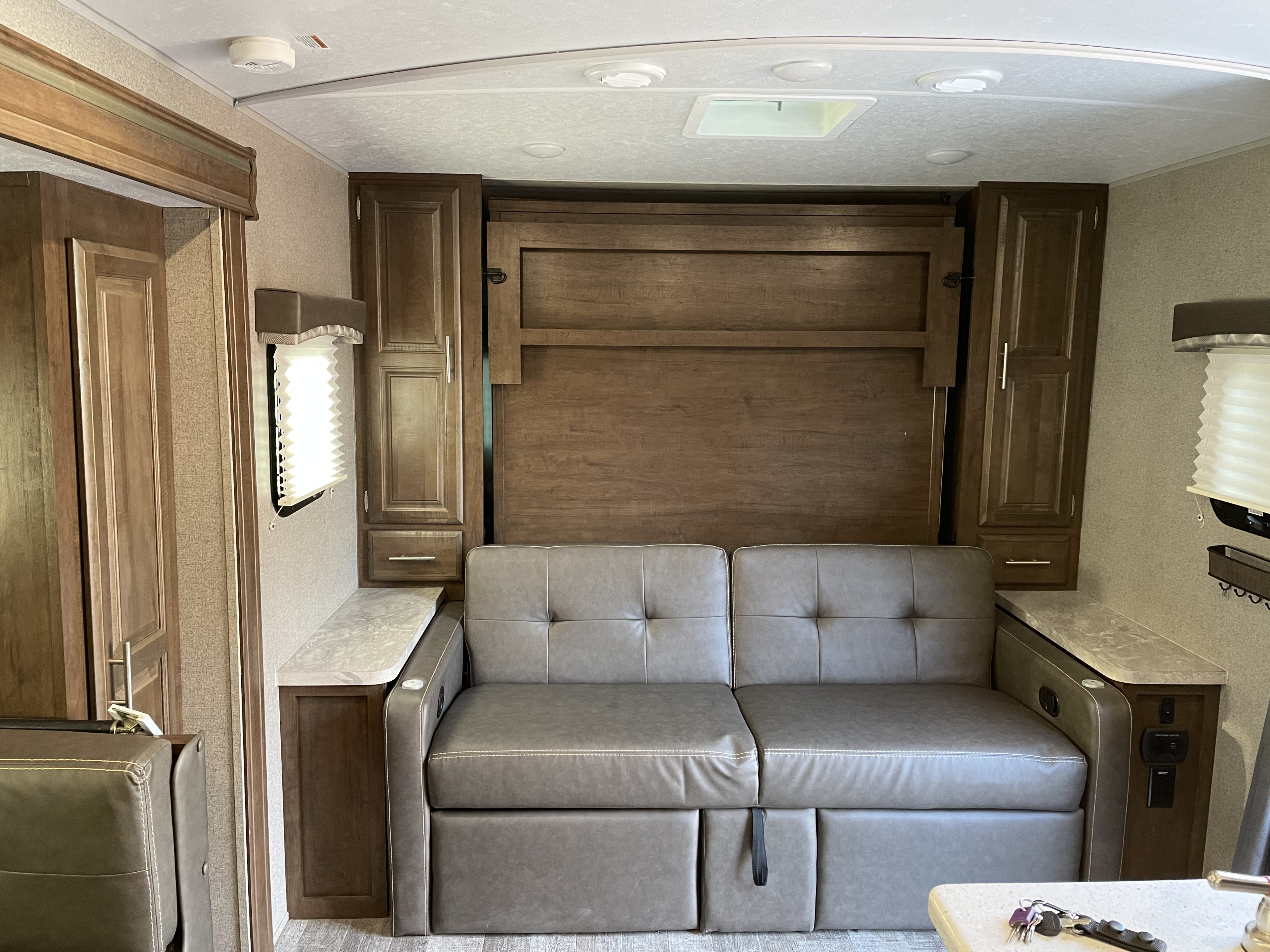RV rental interior: A cozy living space with a grey sofa and a cleverly designed wall bed, surrounded by warm wood cabinets.. Forest River Rockwood Mini Lite 2020
