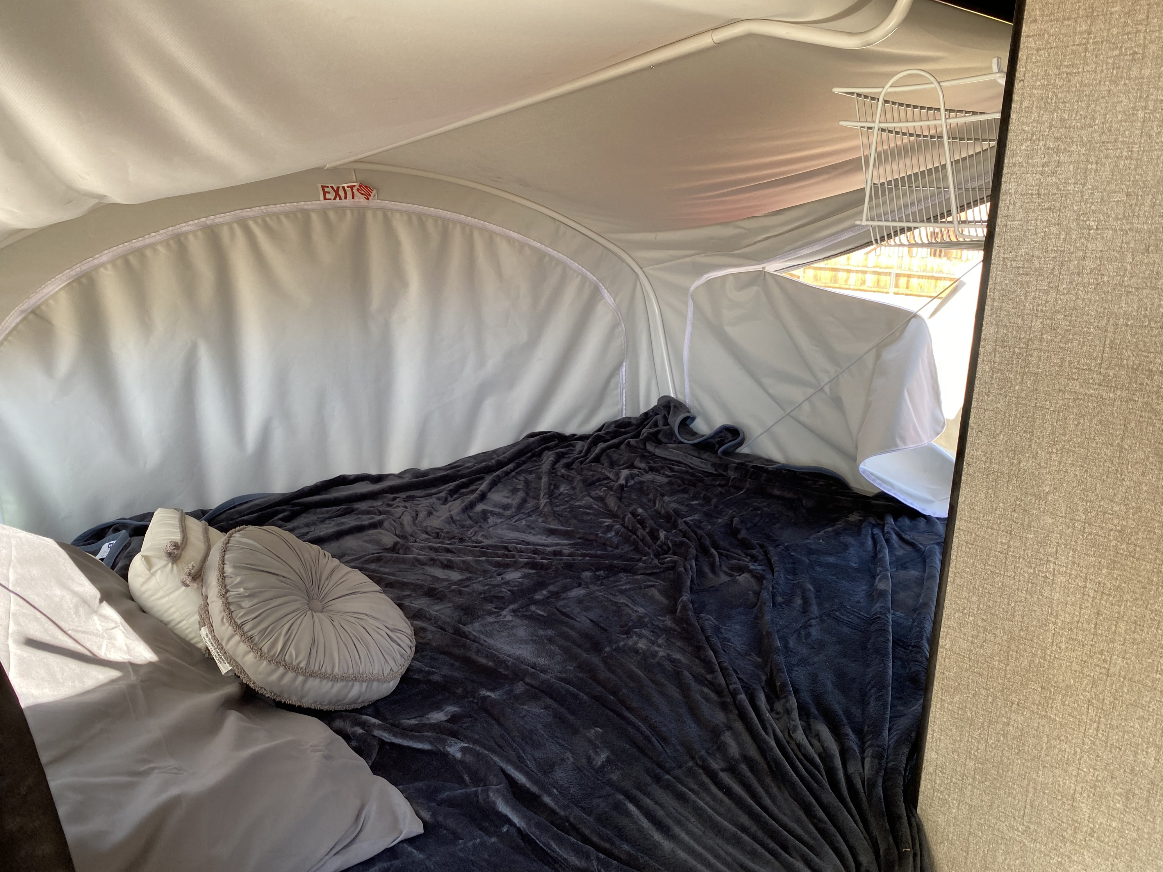 Inside a cozy RV rental pop-up: a comfortable sleeping area with dark blanket, pillows, and an exit sign.. Jayco Jay Feather 2021