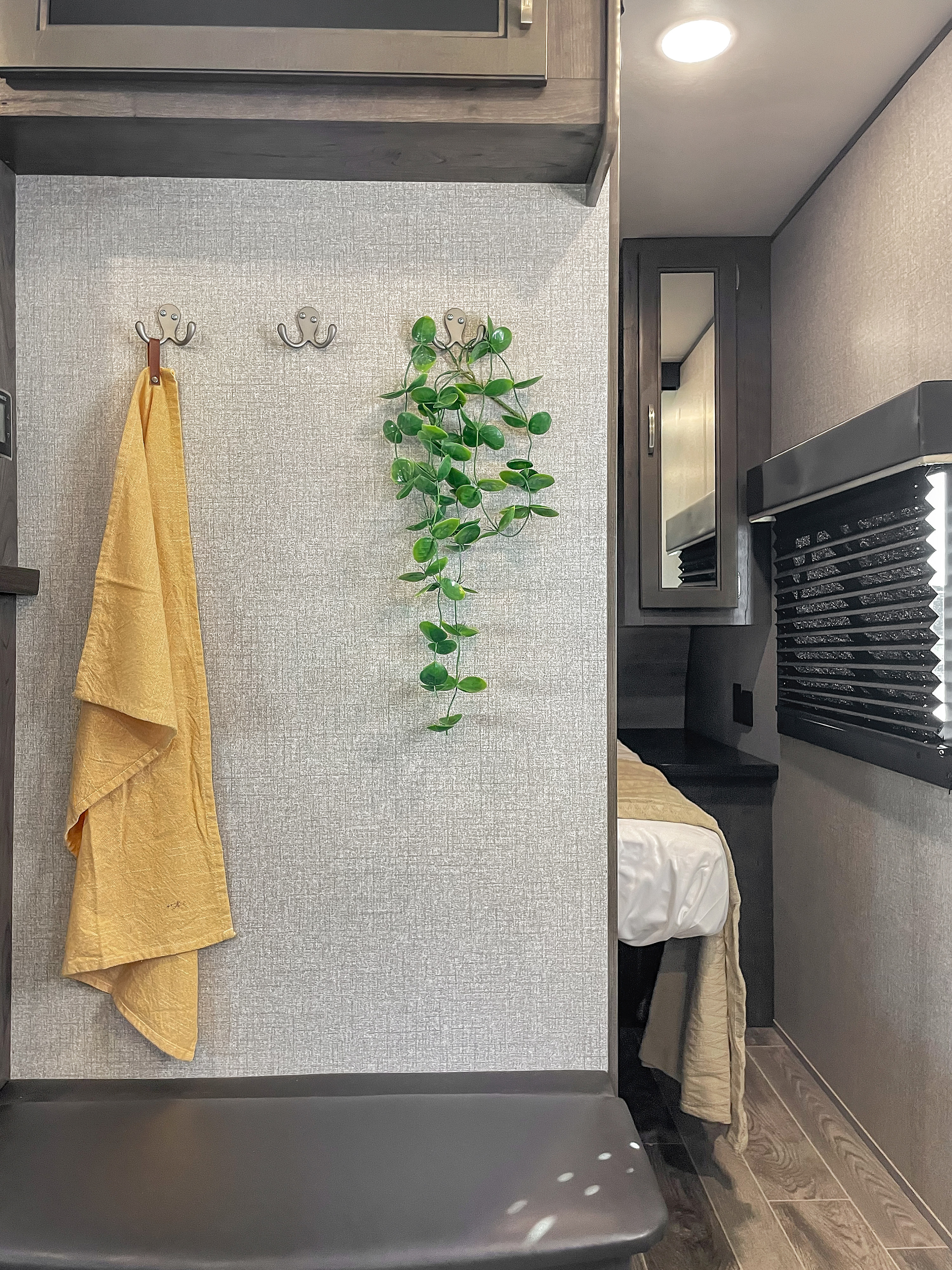 Cozy RV rental interior: grey textured wall with coat hooks, a yellow towel, a faux plant, and a glimpse into a compact bedroom.. Jayco Jay Flight 2021