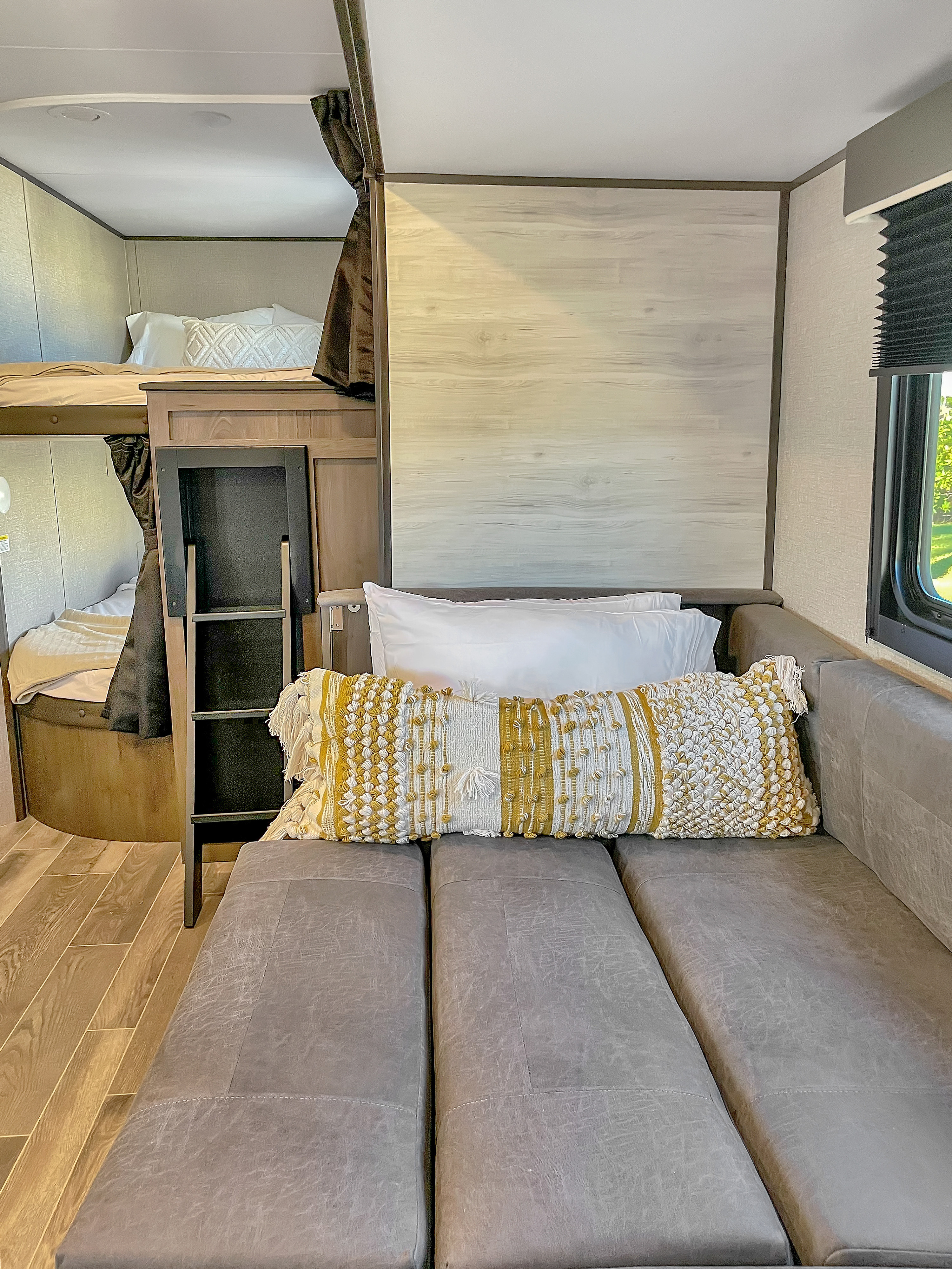 Inside a cozy RV rental: bunk beds with curtains, a ladder, and a long gray sofa with decorative pillows.. Jayco Jay Flight 2021