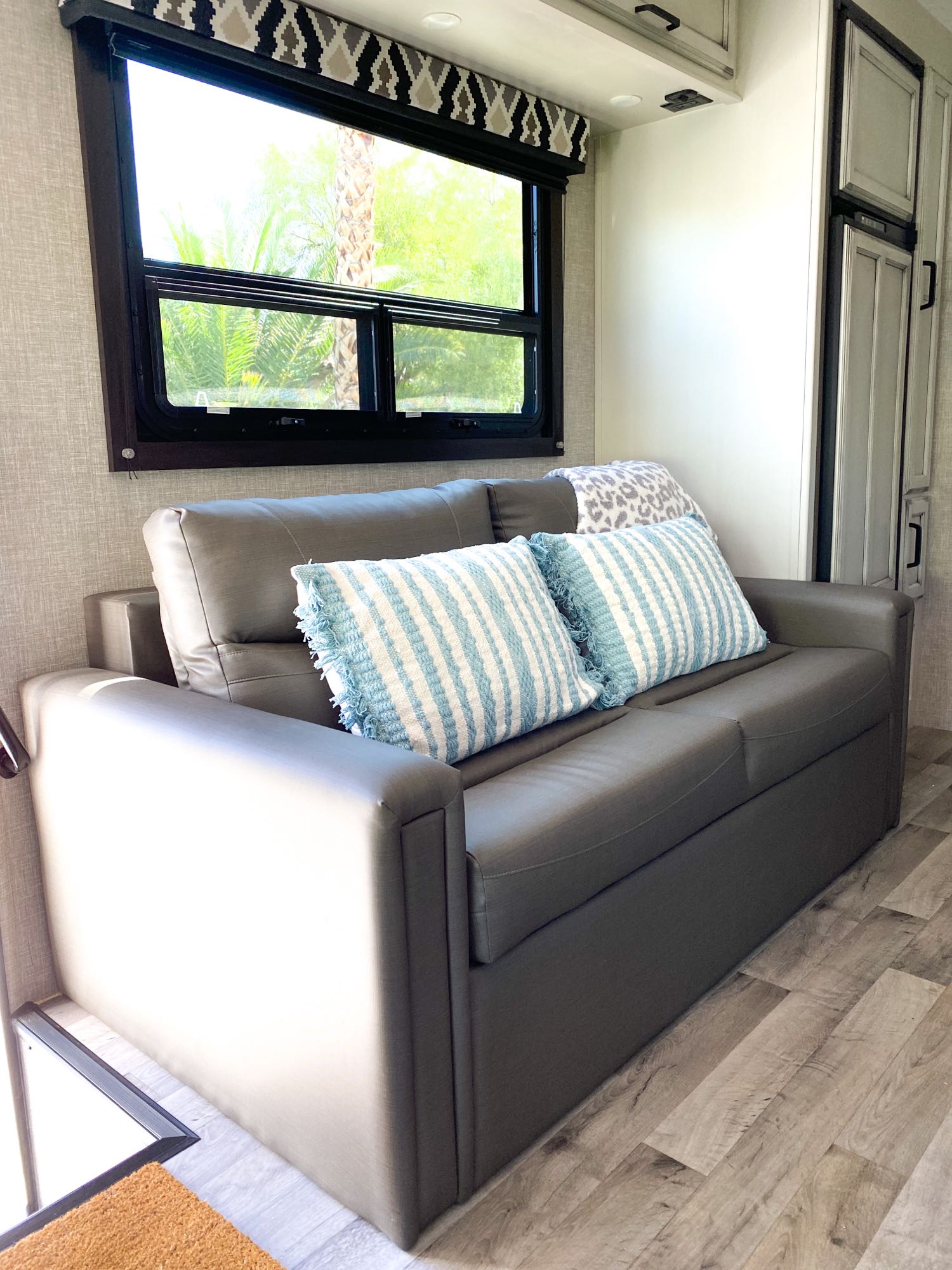Inside an RV rental: a comfortable gray sofa with blue striped pillows, a window with outdoor views.. Entegra Coach Other 2022