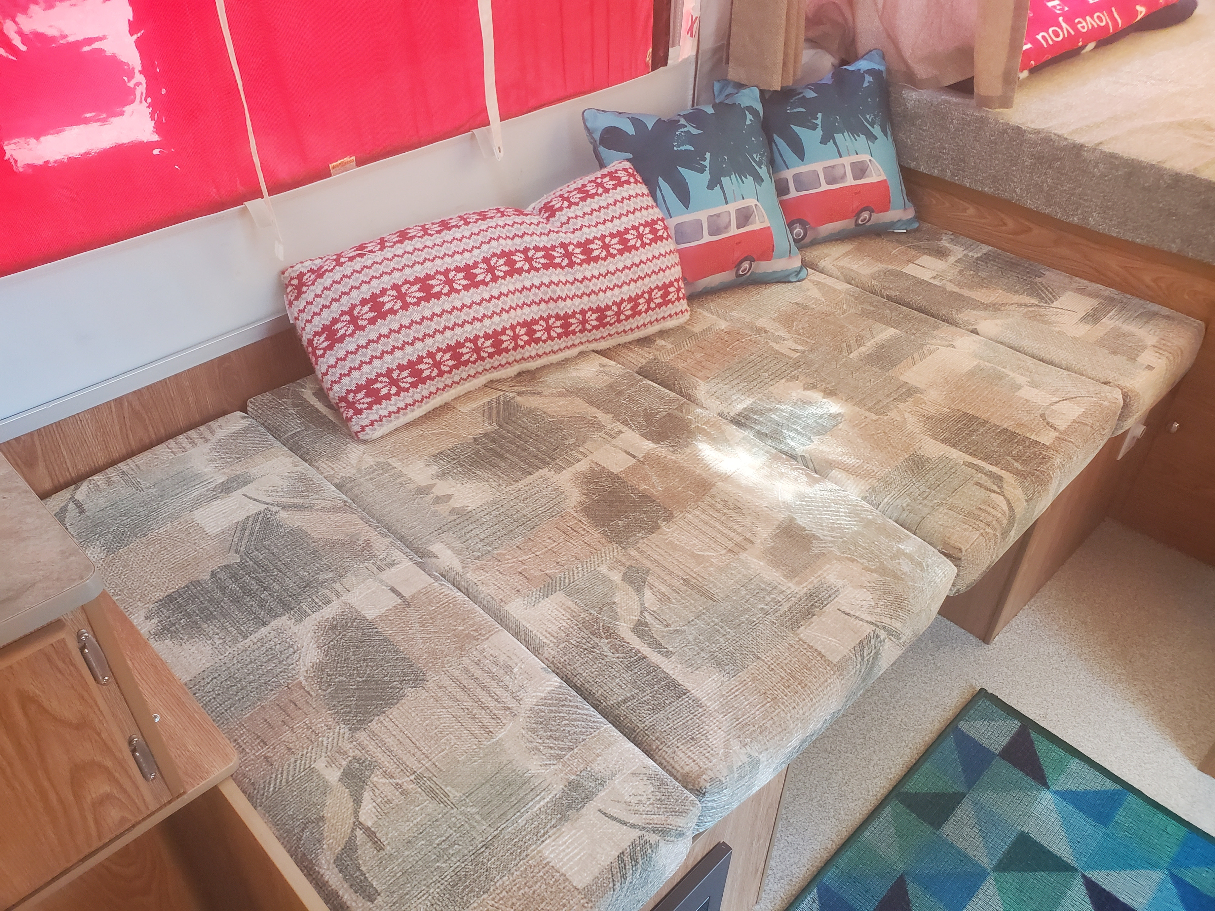 Interior of an RV rental: a compact living area with multi-patterned cushions forming a bench, decorated with red and camper van pillows.. Viking 1906st 2004