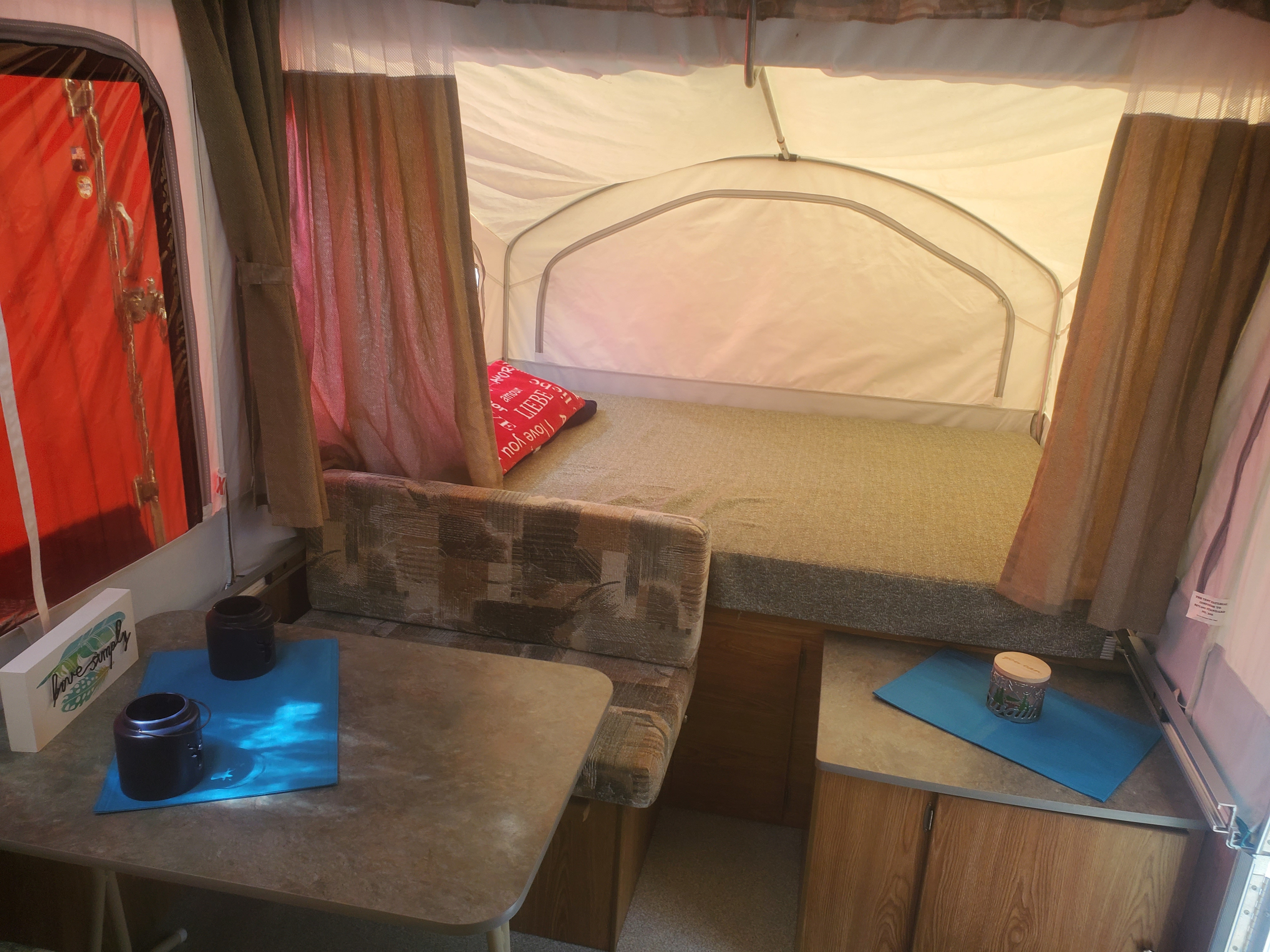 RV rental interior: pop-up camper with bed, dinette, and "live simply" sign. Your cozy camping experience awaits!. Viking 1906st 2004