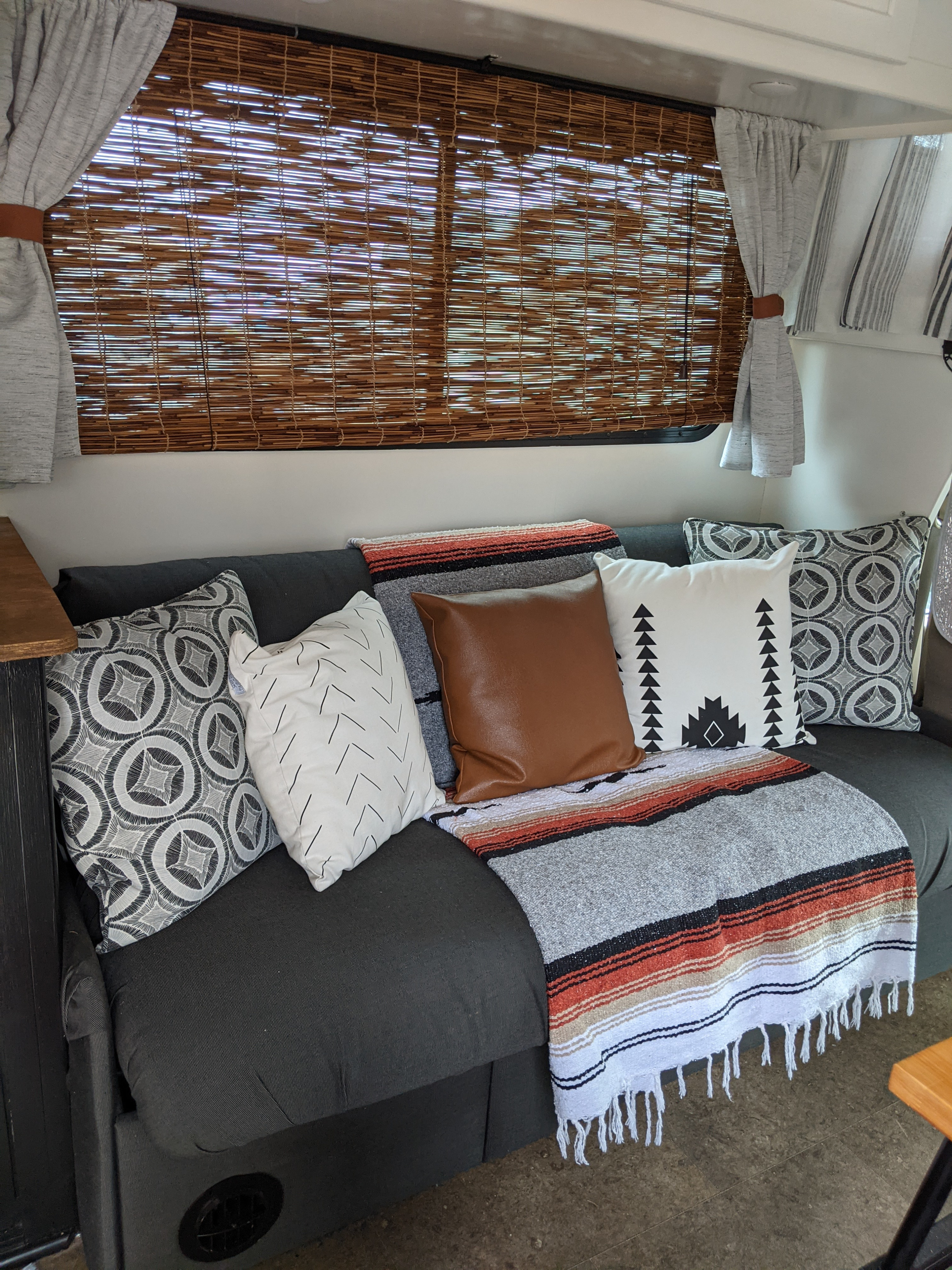 Cozy RV rental interior featuring a dark gray couch, patterned throw pillows, a vibrant blanket, and bamboo window blinds.. Winnebago Minnie Winnie 2016
