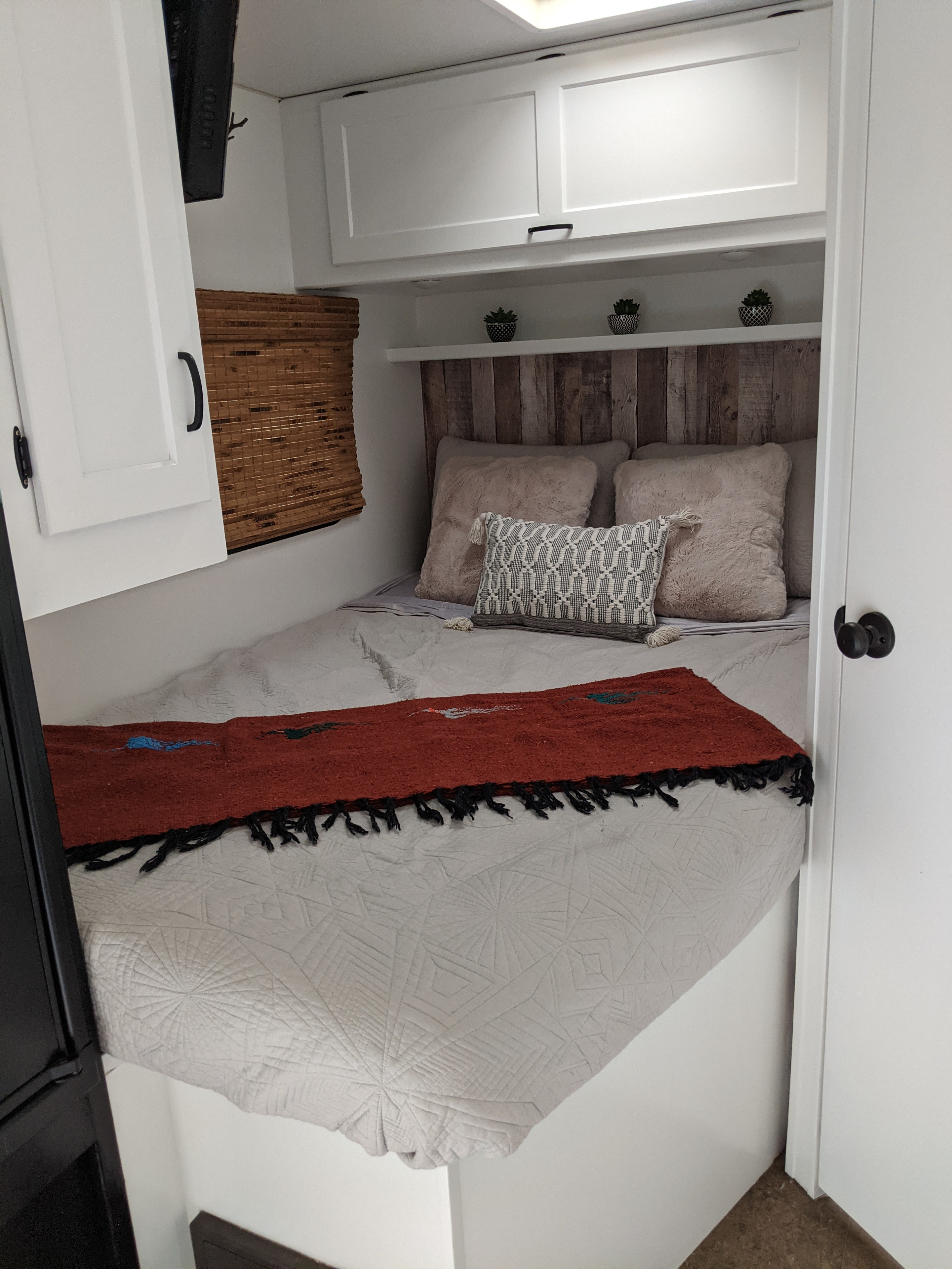 Cozy RV rental bedroom featuring a bed with a rustic headboard, soft bedding, and overhead storage, ideal for comfortable travel.. Winnebago Minnie Winnie 2016