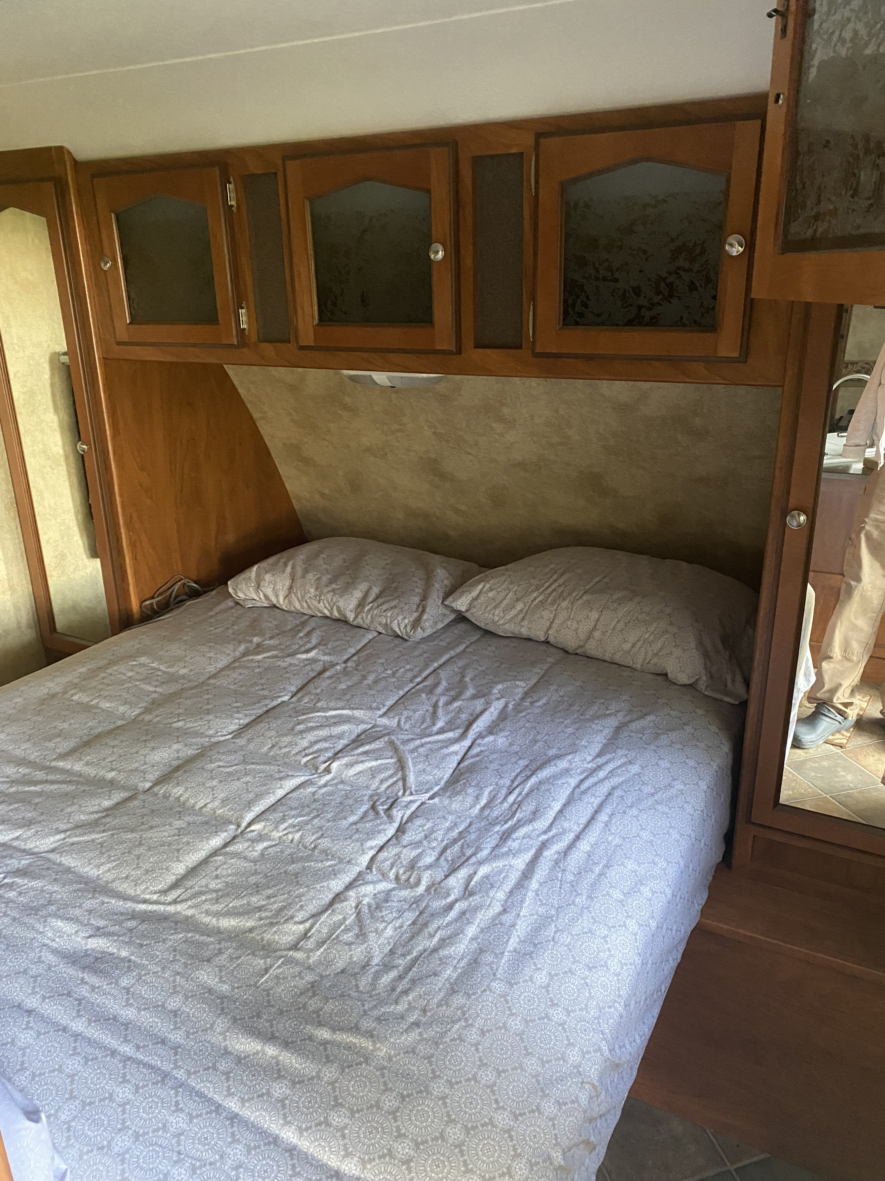 RV rental bedroom with patterned bed, two pillows, wooden overhead cabinets, and a side mirror.. Other Passport 2012