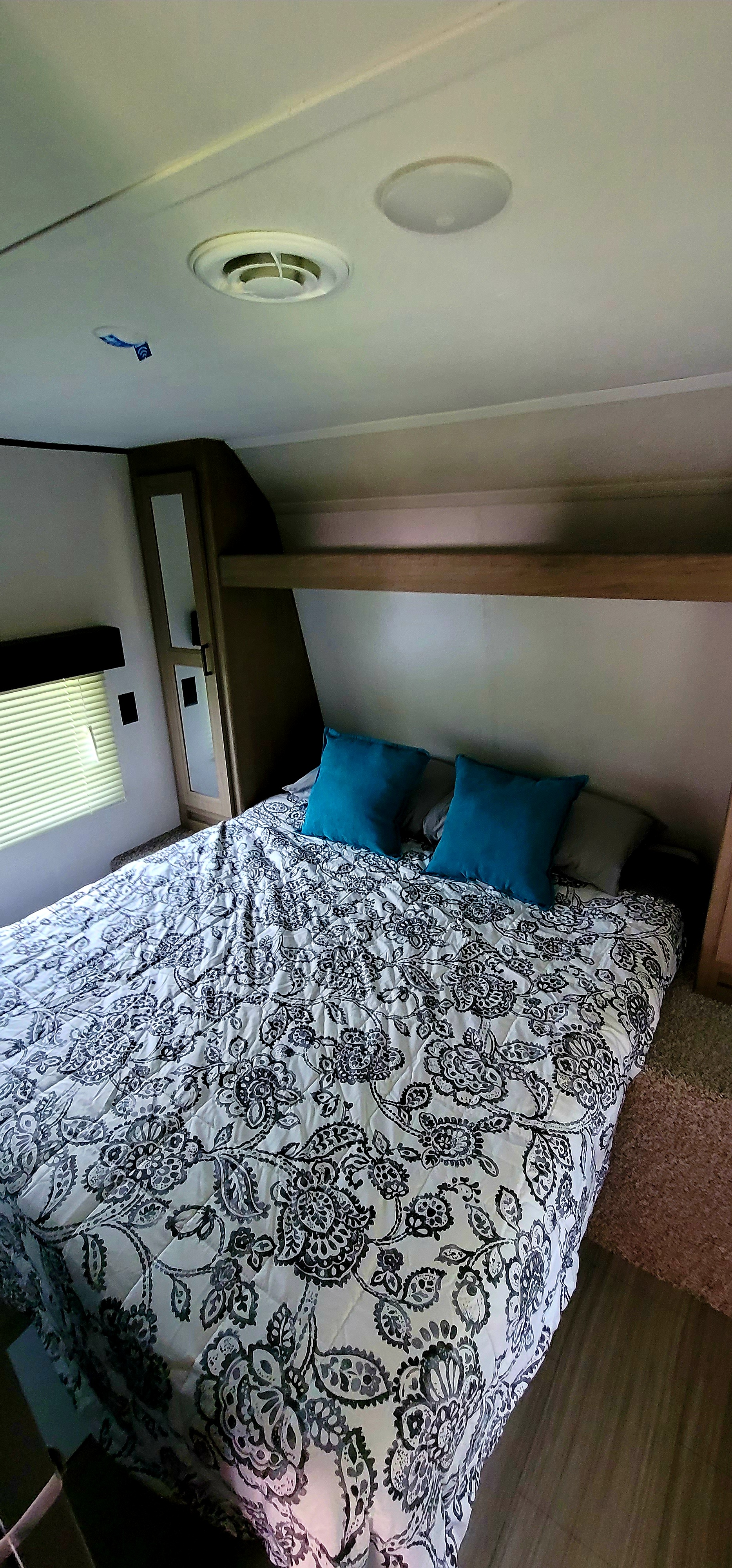 RV rental bedroom interior featuring a comfortable bed with a patterned comforter, blue pillows, and a window.. Keystone Hideout 2021