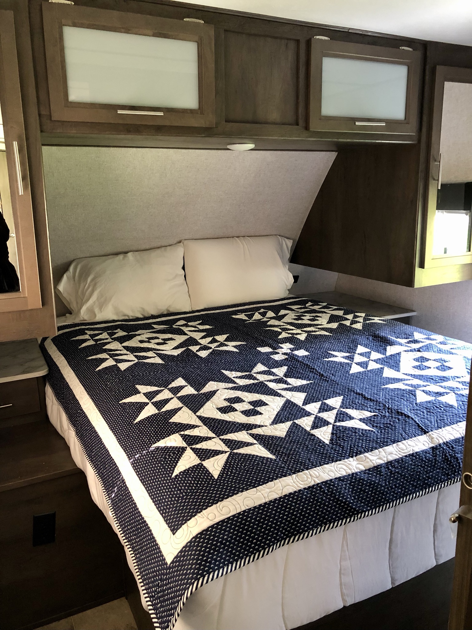 Experience comfort in your RV rental! This bedroom features a plush bed, blue quilt, and practical overhead storage.. Coleman Other 2021