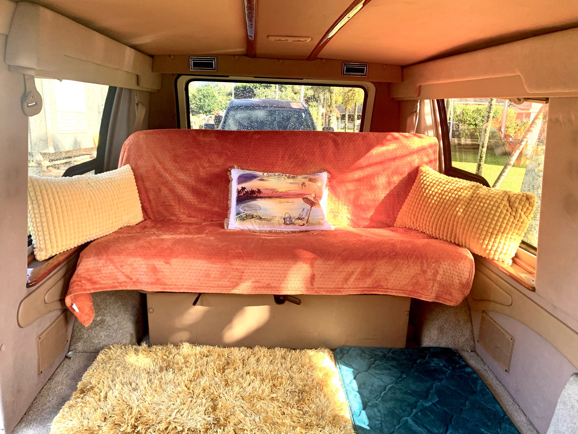 Cozy RV rental interior featuring an orange bench bed with pillows and soft floor mats, ready for travel adventures.. Dodge Ram 1500 1999