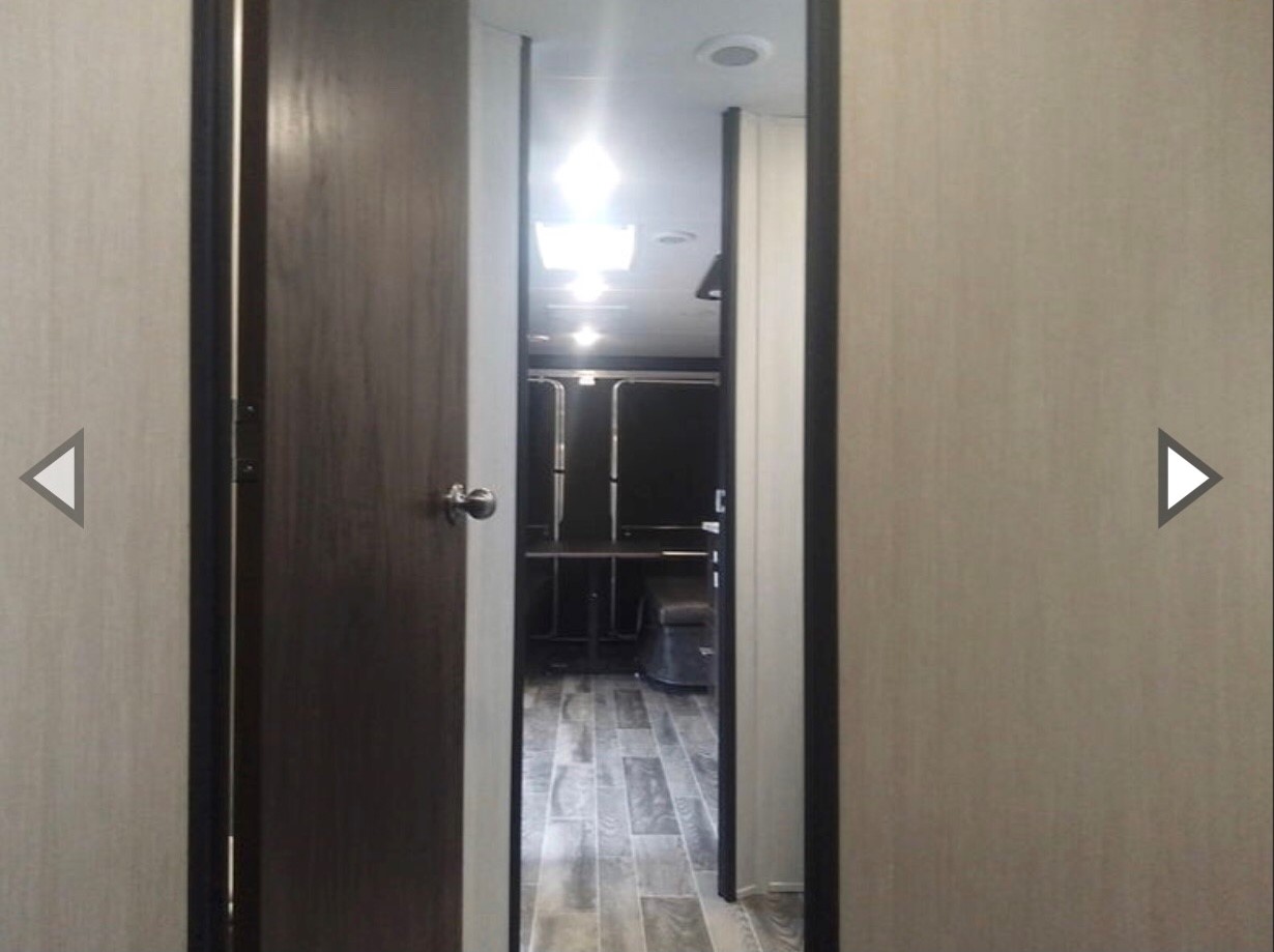 RV rental view: An open door reveals a practical, bright interior with wood-look flooring, hinting at a bunk or storage area.. Forest River Cherokee Grey Wolf 2019