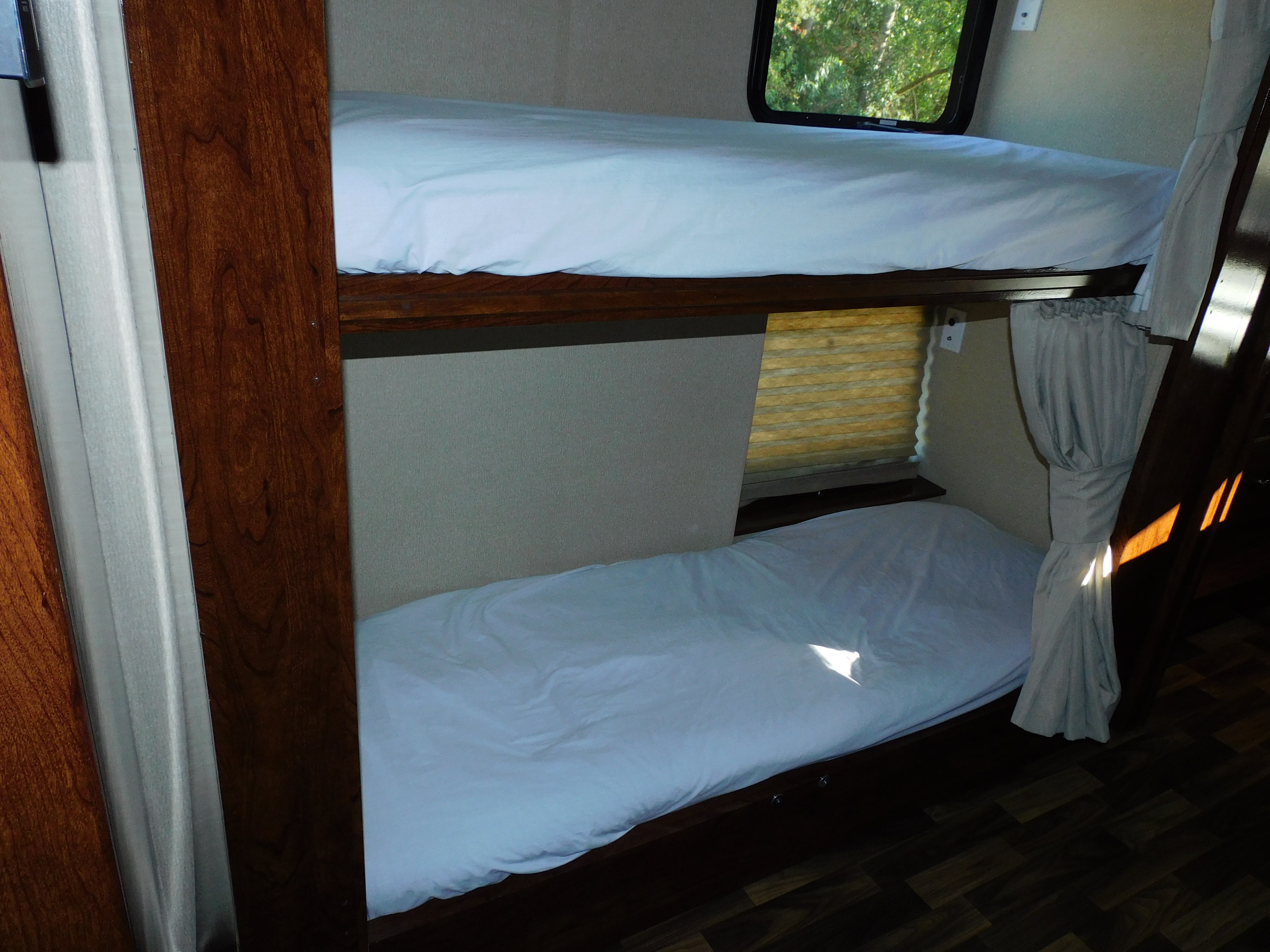 Inside an RV rental: two neatly made bunk beds with white sheets, featuring windows for light and views.. Coachmen Pursuit 2017
