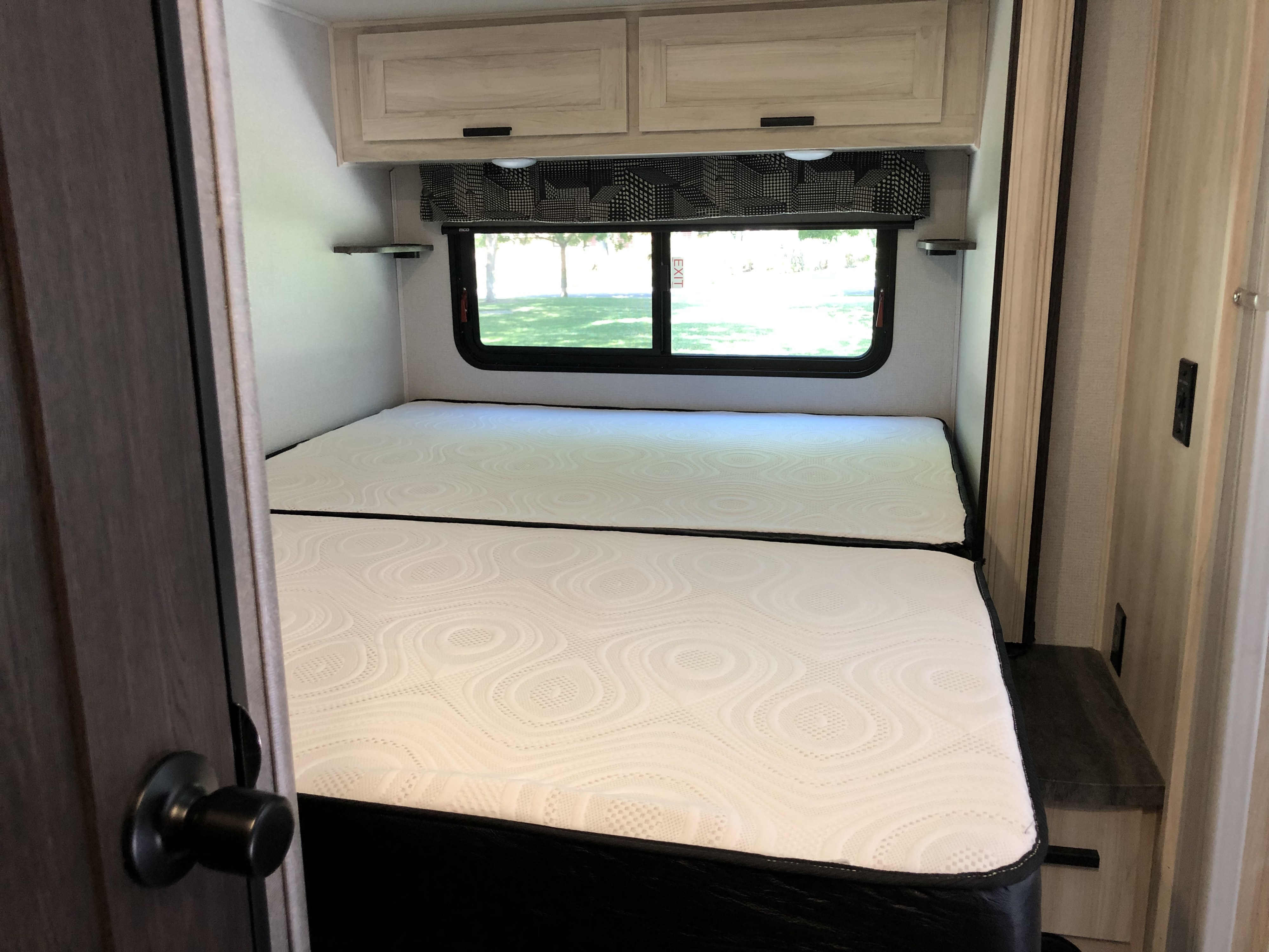 Spacious RV rental bedroom featuring two side-by-side mattresses, overhead storage, and a large window overlooking nature.. Forest River Sunseeker 2021