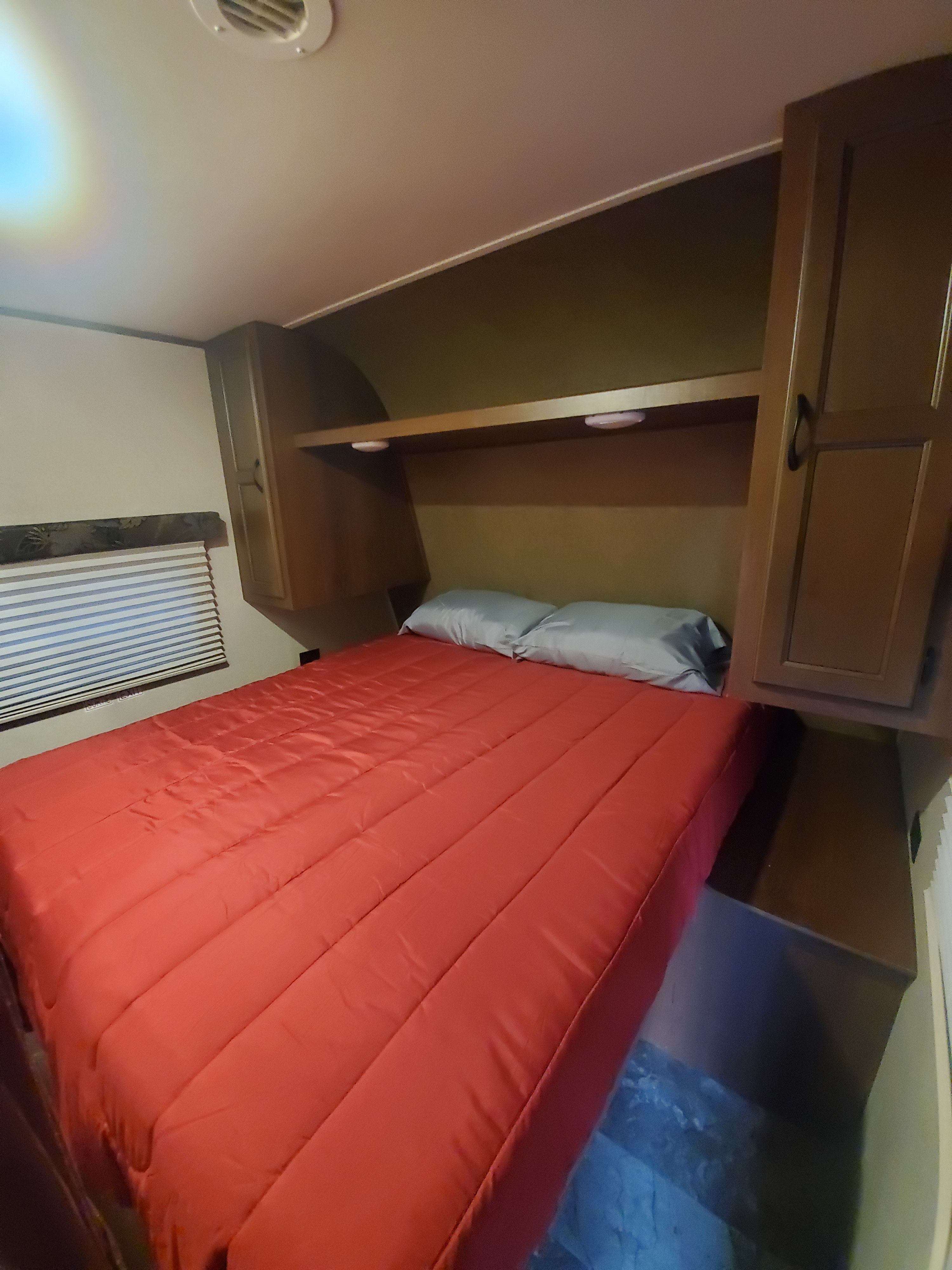 RV rental bedroom with red comforter, gray pillows, overhead cabinets, and window blinds.. Jayco Jay Flight SLX 2015