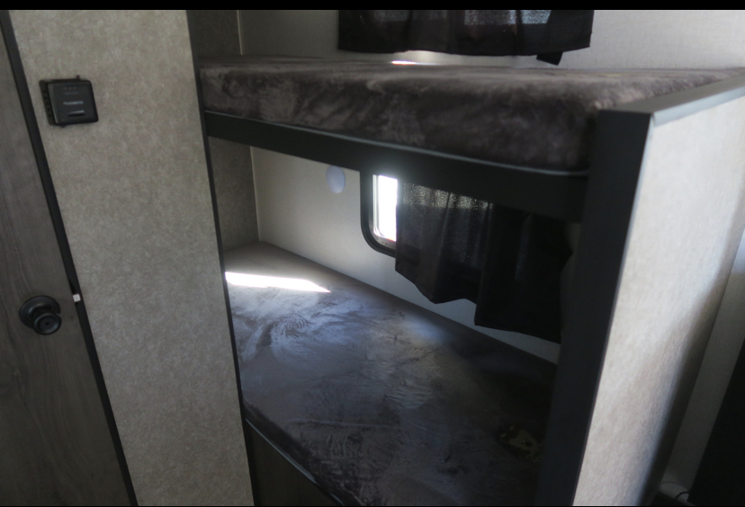 RV rental's cozy interior features comfortable bunk beds with dark mattresses. A window with curtains provides natural light to the lower bunk.. Highland Ridge RV Open Range 2021