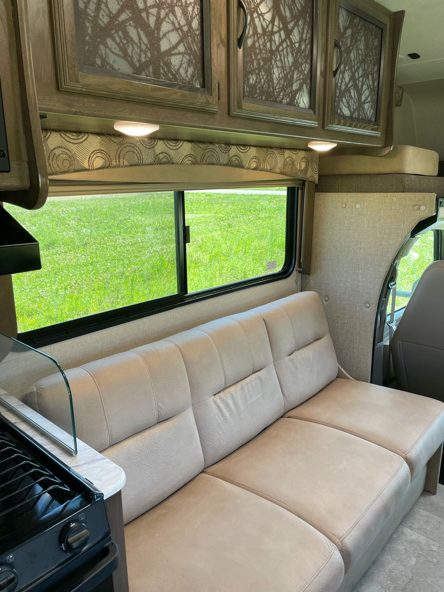 Cozy RV rental interior with a comfy sofa, bright kitchen, and large window showcasing lush green views outside.. Coachman Freelander 2019