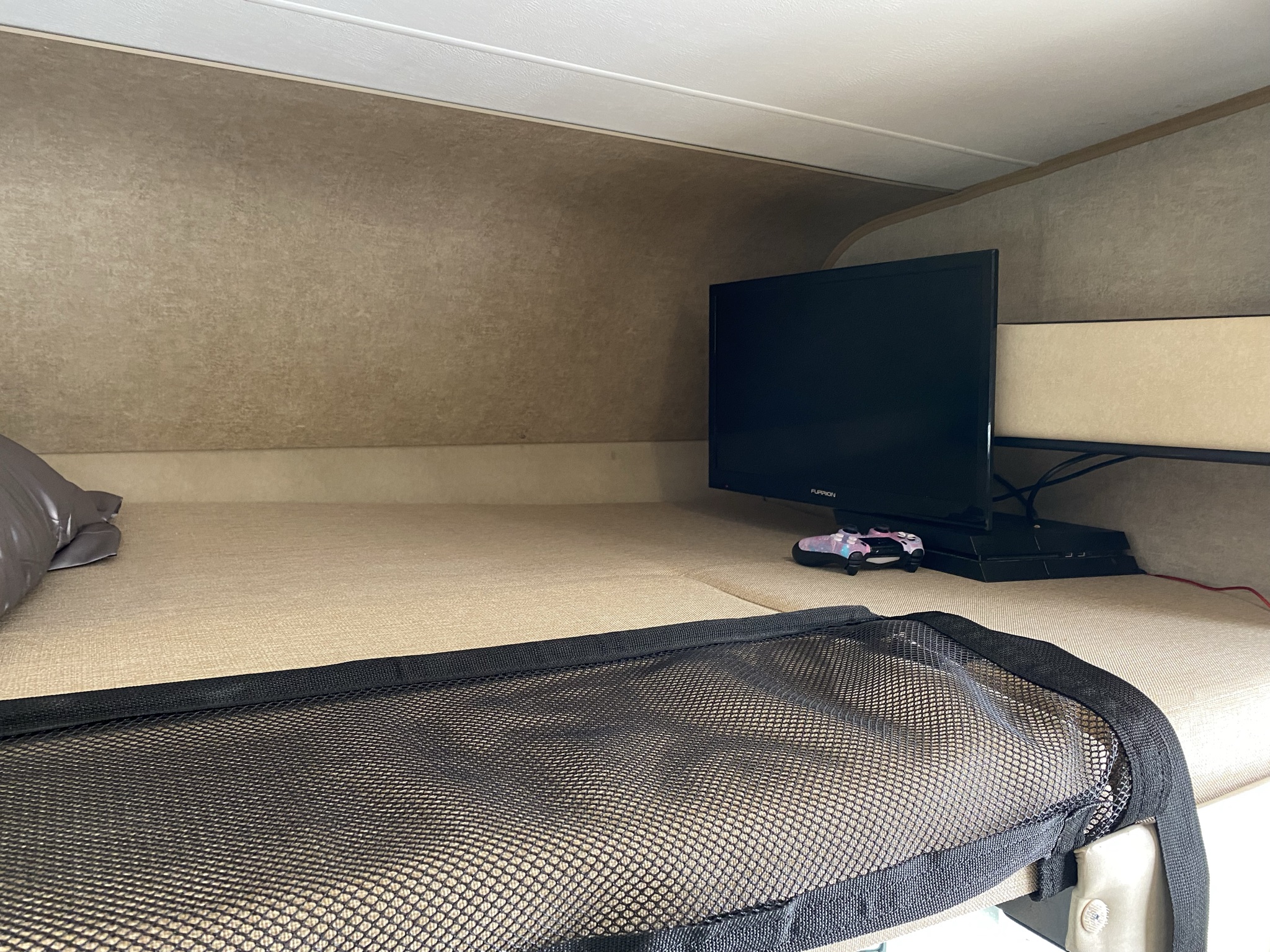 A view inside an RV rental's bunk, showing a TV, gaming setup, and safety net for comfortable travel.. Coachmen Prism 2016