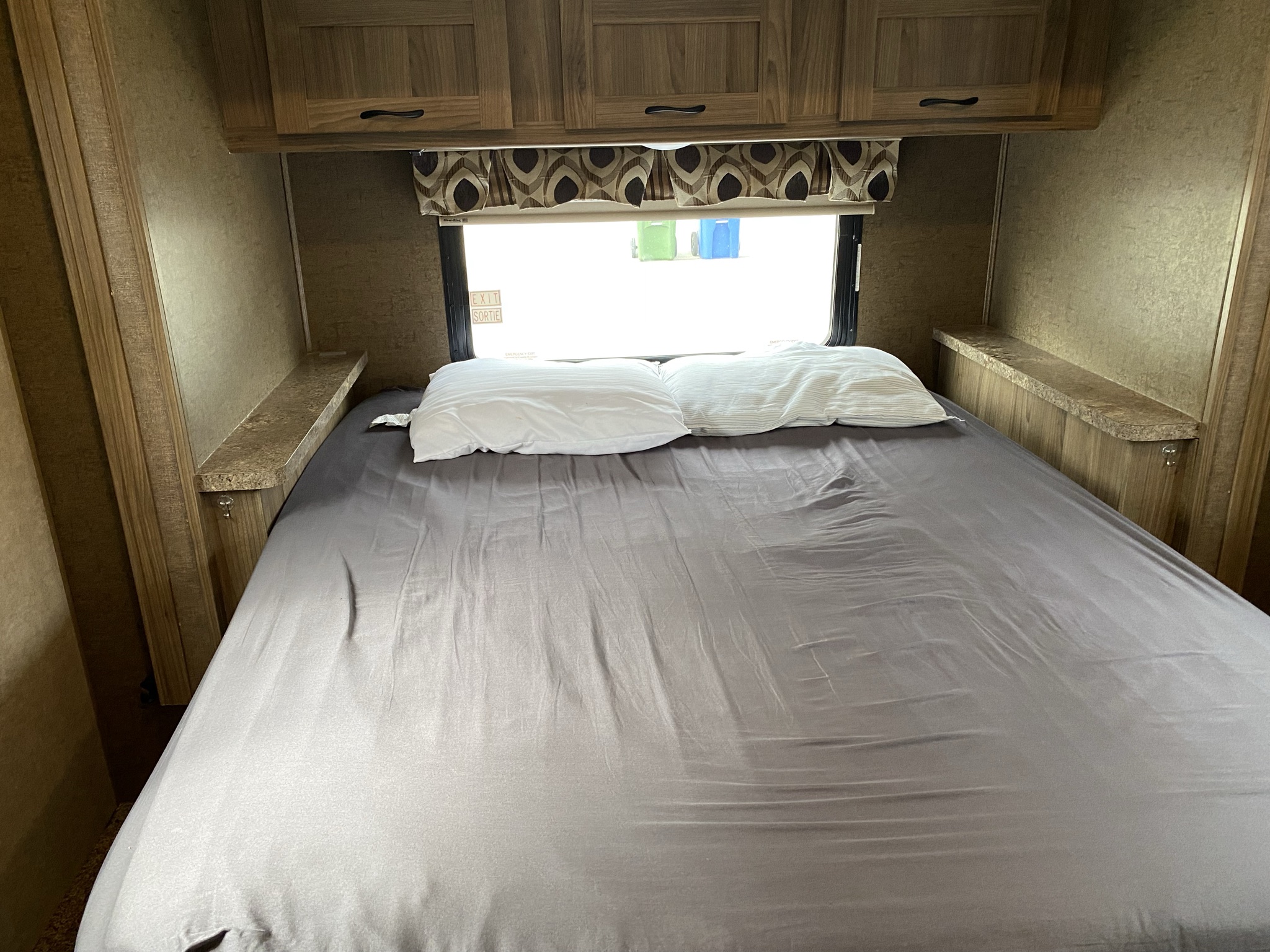 RV rental bedroom featuring a comfortable bed, white pillows, overhead cabinets, and a window.. Coachmen Prism 2016