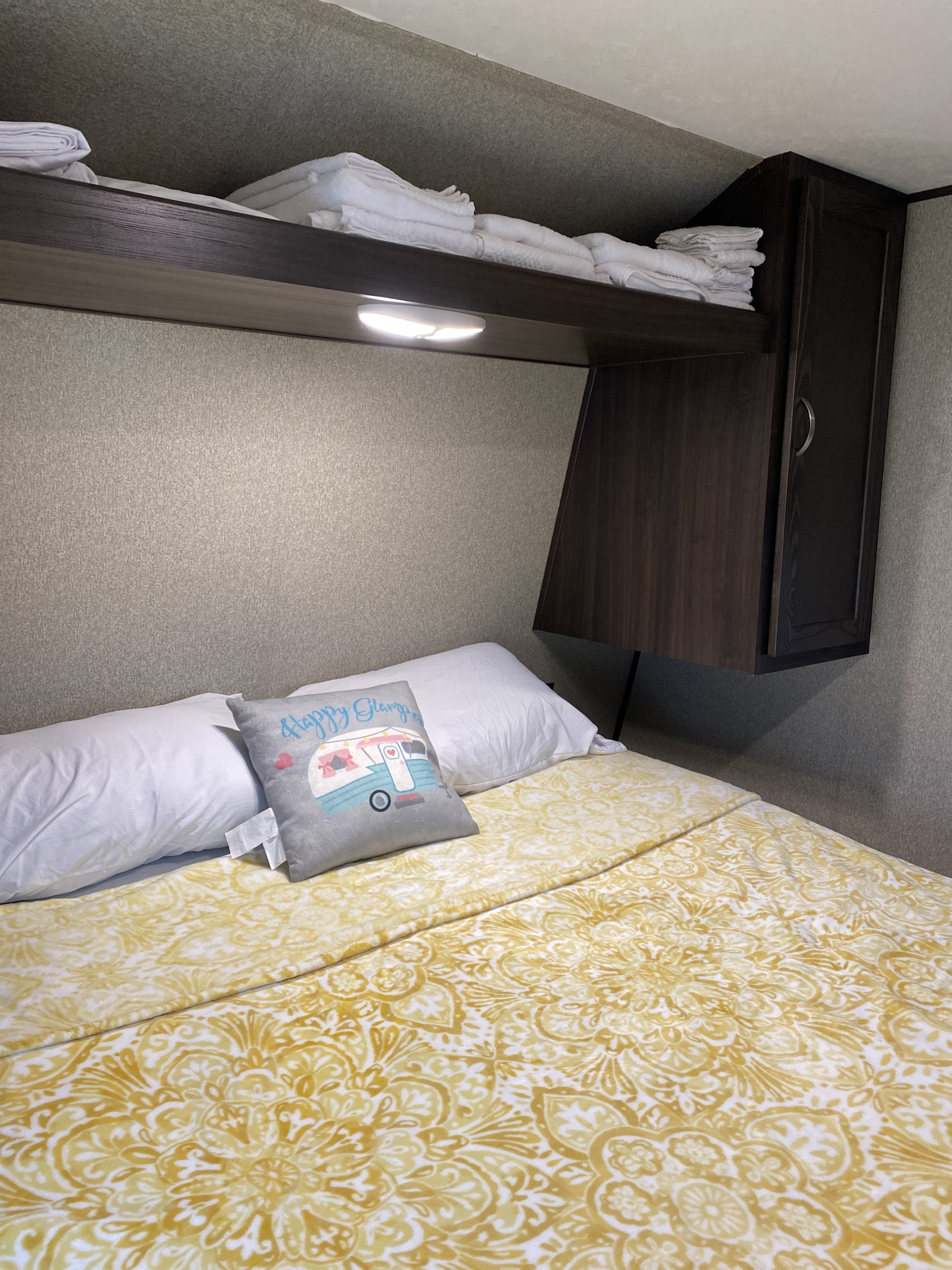 Cozy RV rental bedroom with yellow patterned bedding, white pillows, and overhead shelving for storage.. Keystone Springdale 2018